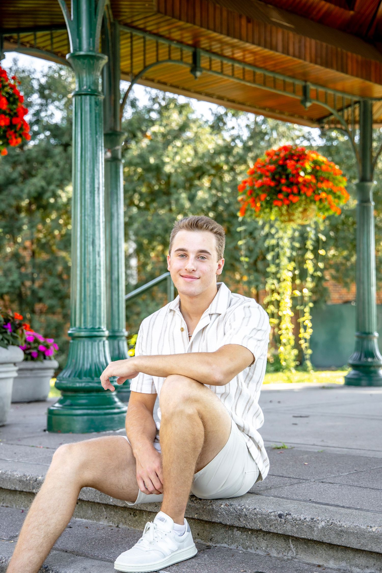 Young man in striped shirt relaxes on outdoor porch with green columns and red flowers.