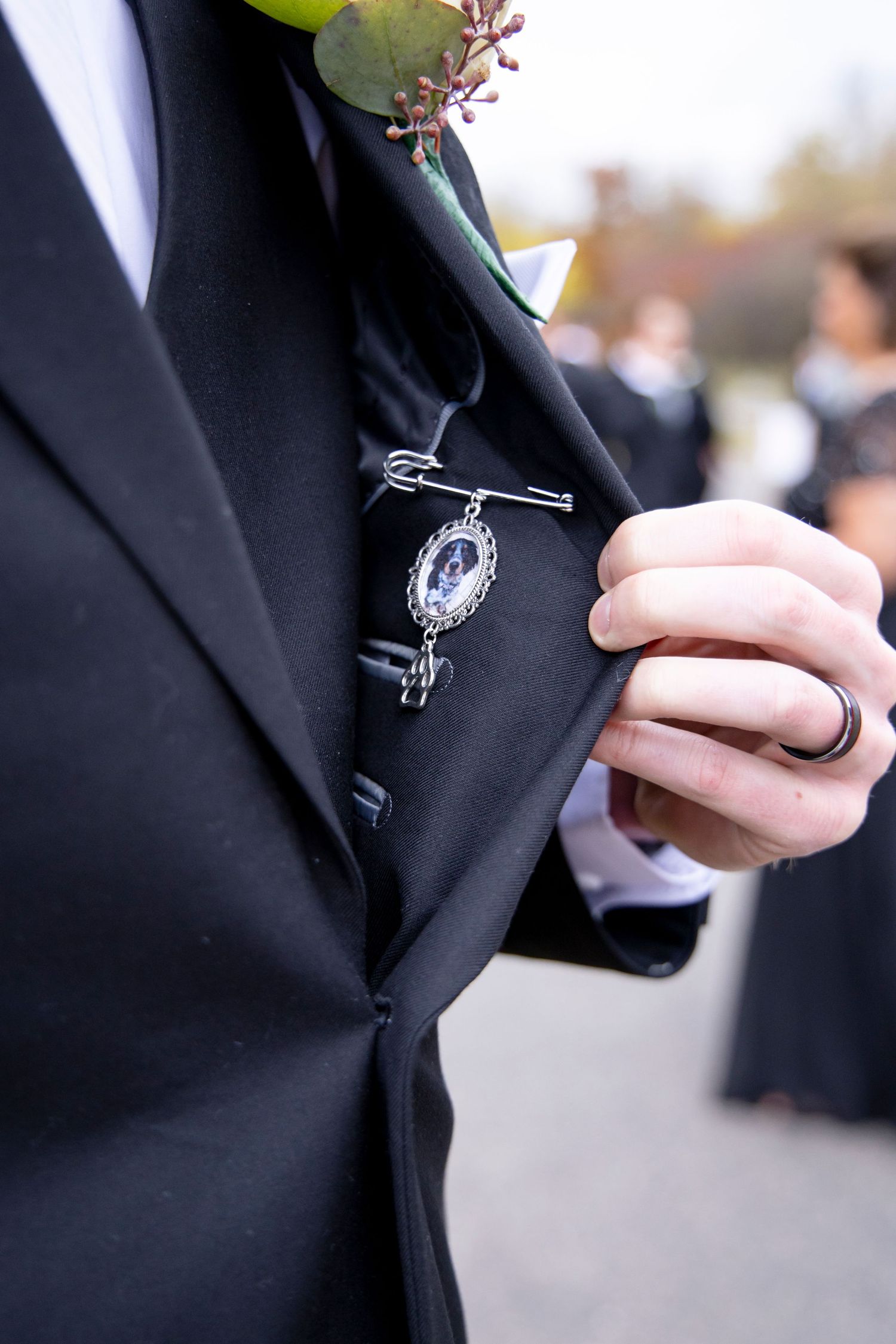 Close-up of groom's boutonniere and decorative pin on black suit lapel.