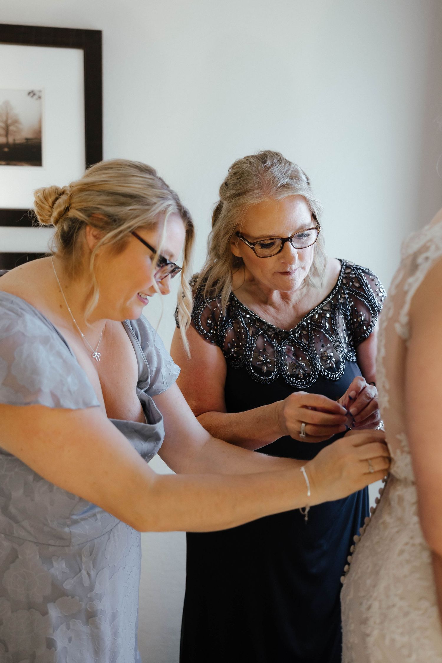 Two people helping with wedding dress preparations in a brightly lit room.