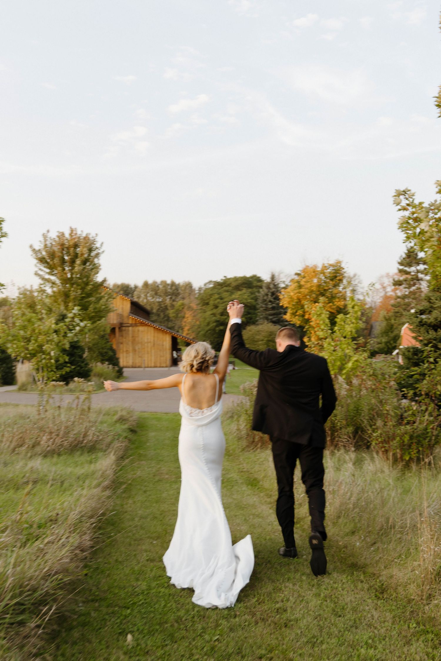 Joyful couple walking through field with raised arms in celebration.