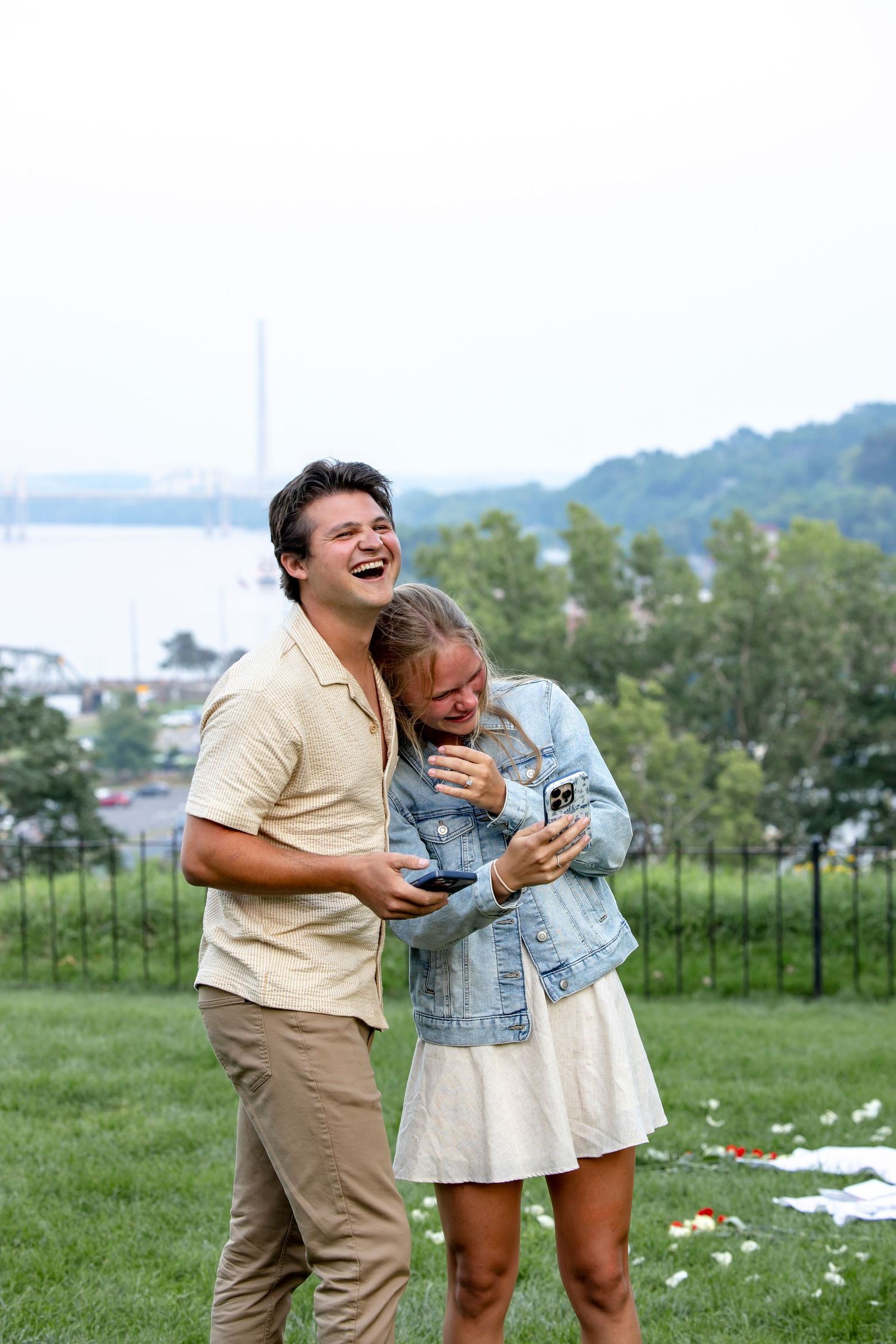 A couple laughs together during an outdoor picnic on a grassy hill.