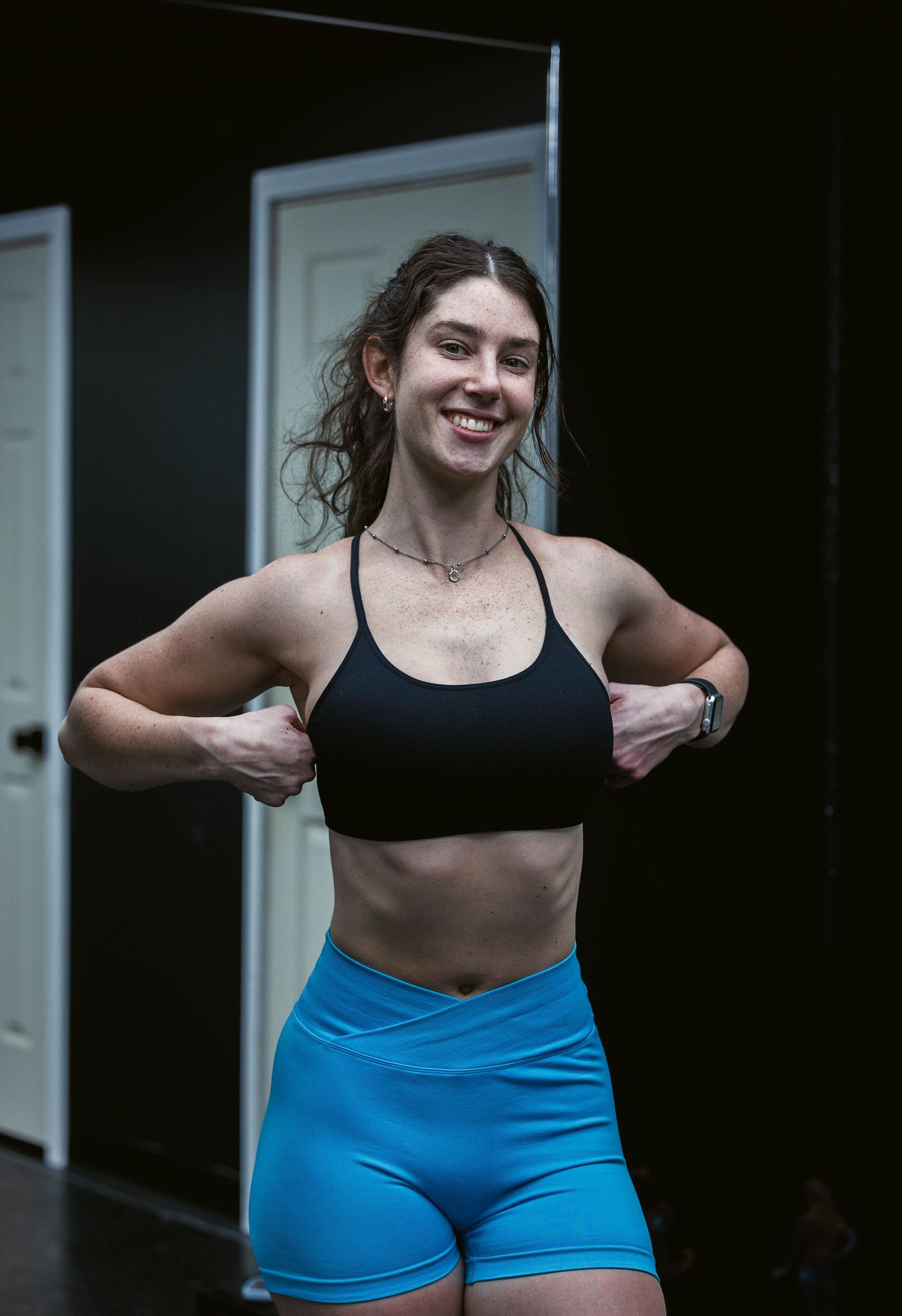 A woman in athletic wear smiles while working out in a dark gym setting.