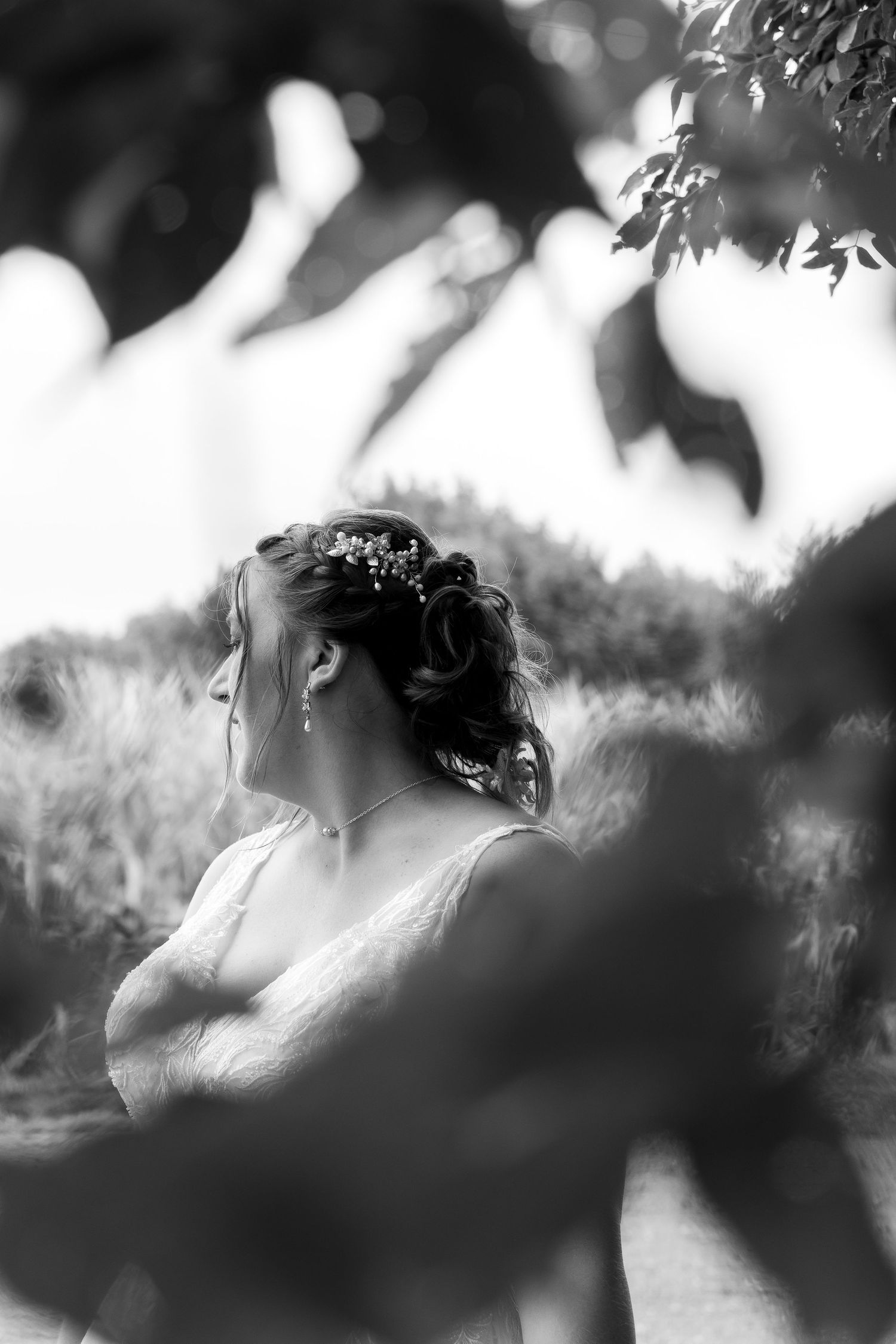 Artistic black and white portrait through leaves and branches at outdoor wedding.