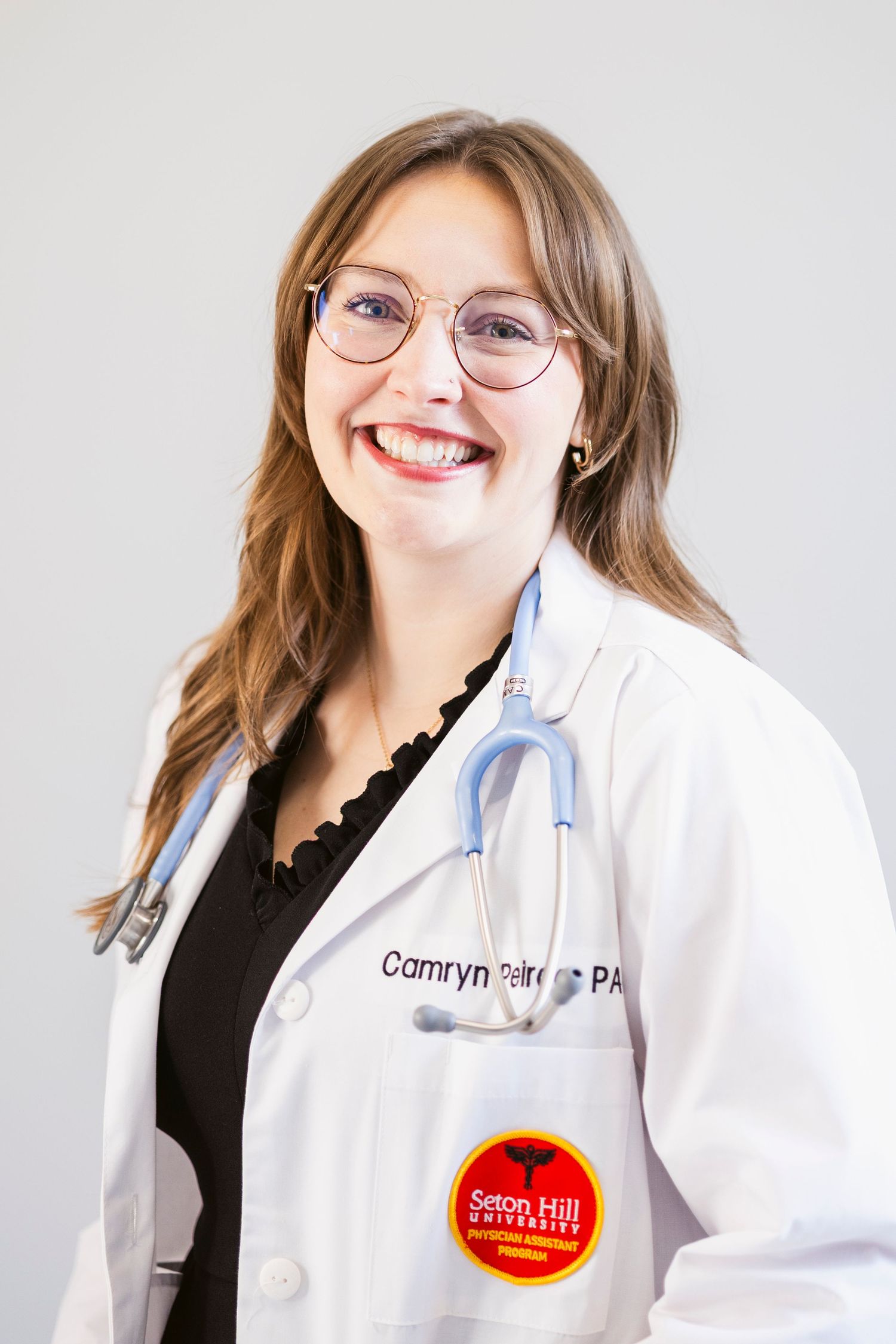 Medical professional wearing glasses and white coat smiles warmly in studio portraits.