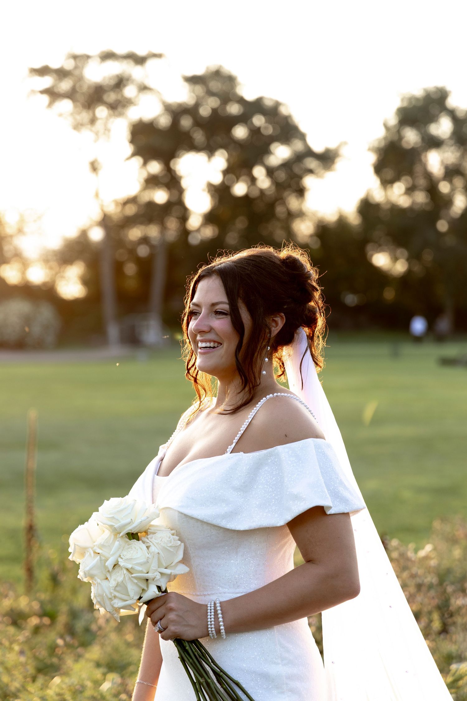 Bride holding white bouquet in golden sunset light during outdoor wedding.
