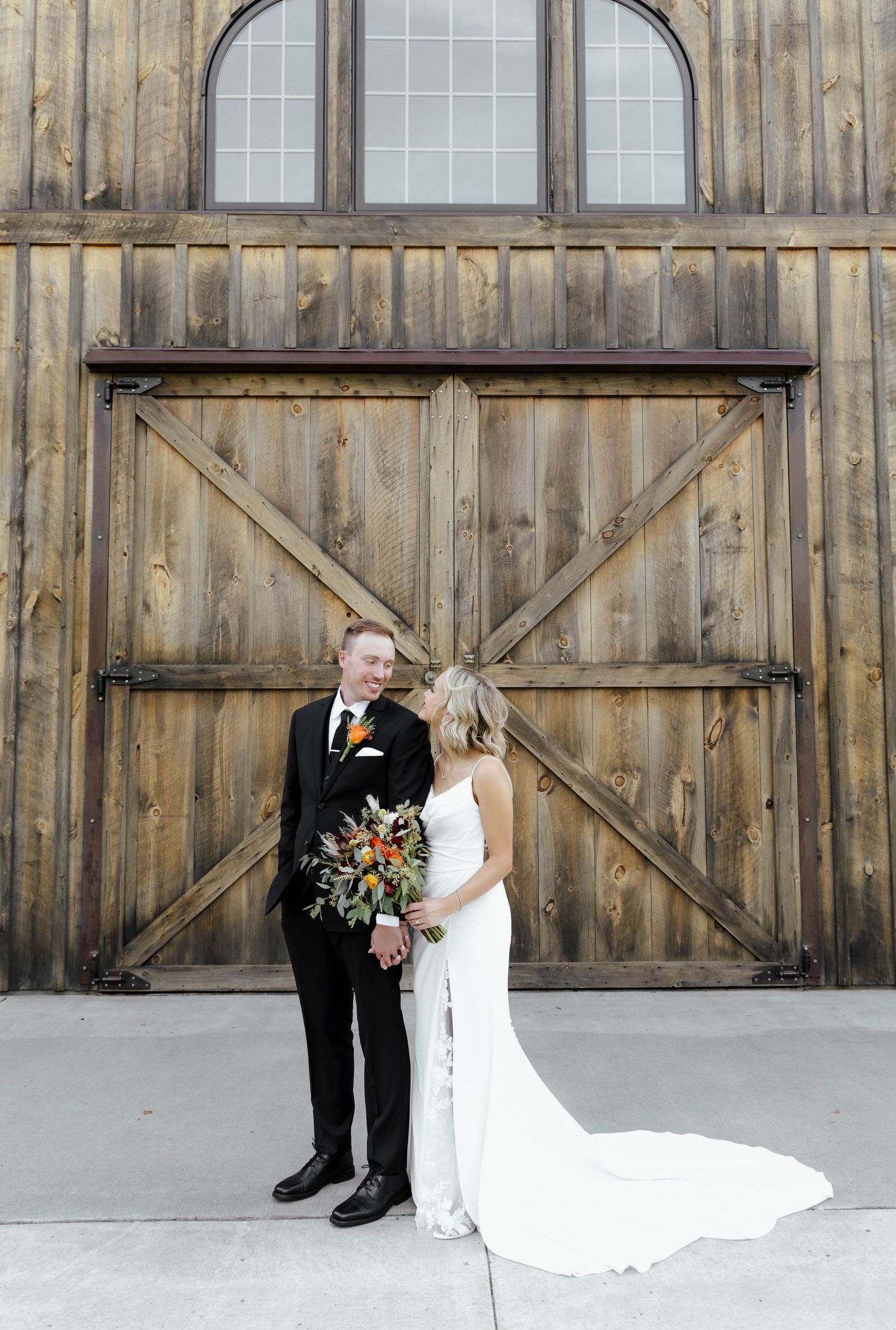 Wedding couple posing in front of a rustic wooden barn with large windows.