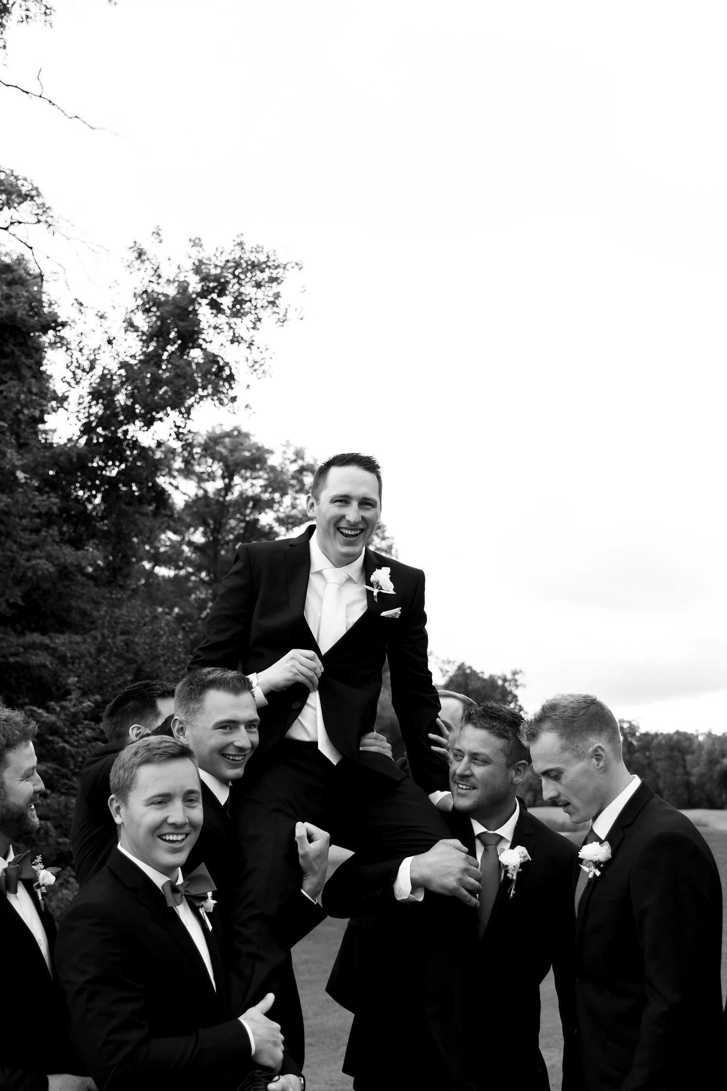 A black and white photo of groomsmen celebrating at an outdoor wedding.