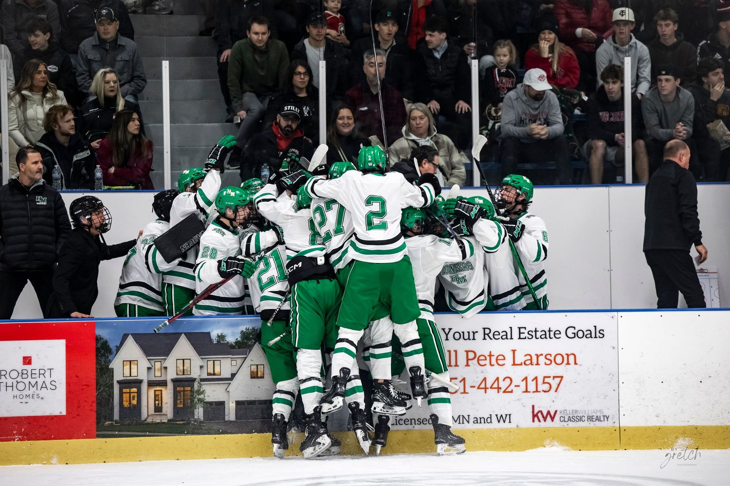 Hockey team in green jerseys celebrates a goal with teammates near the boards.