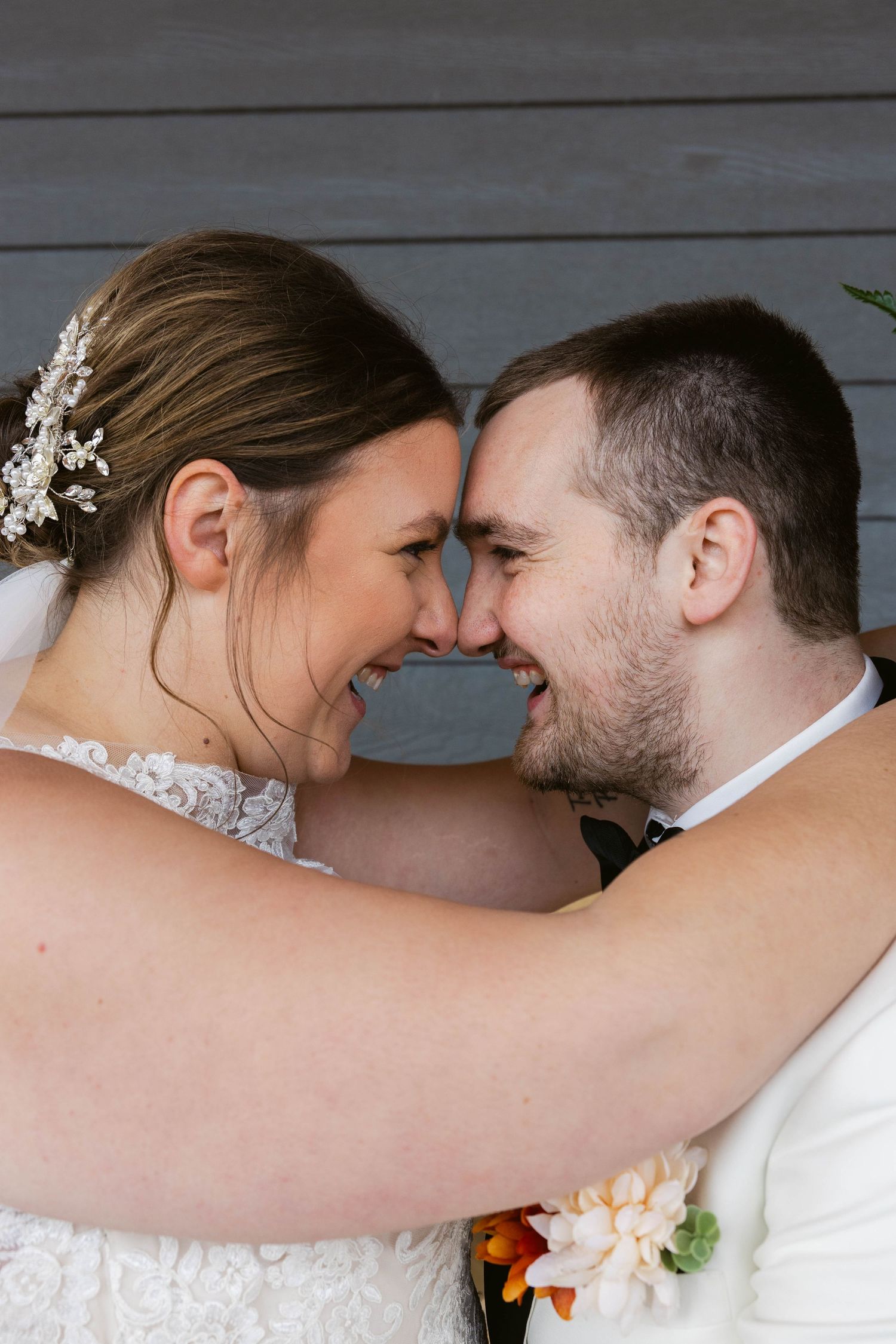 Intimate wedding portrait showing joy and laughter against wooden backdrop.