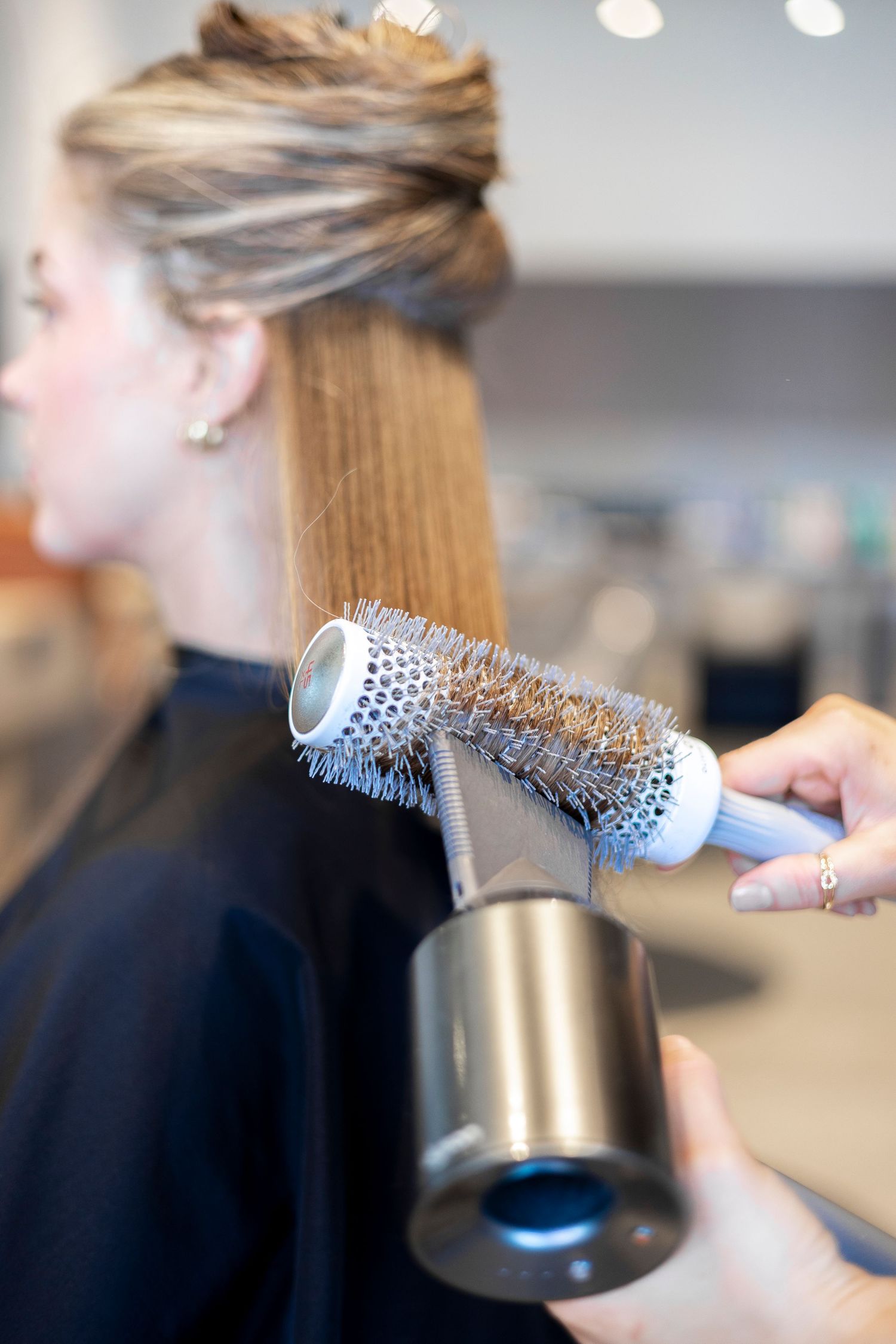 Close-up of round brush being used to style hair section during professional blowout.