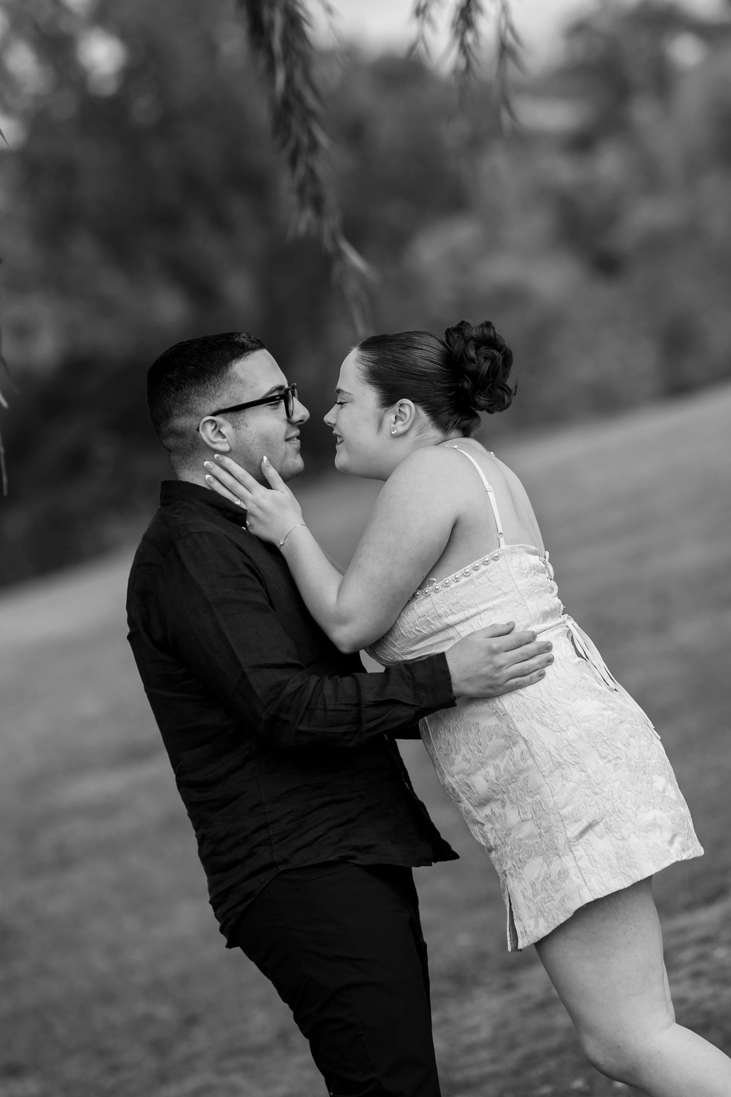 Black and white romantic moment between newlyweds under a willow tree.