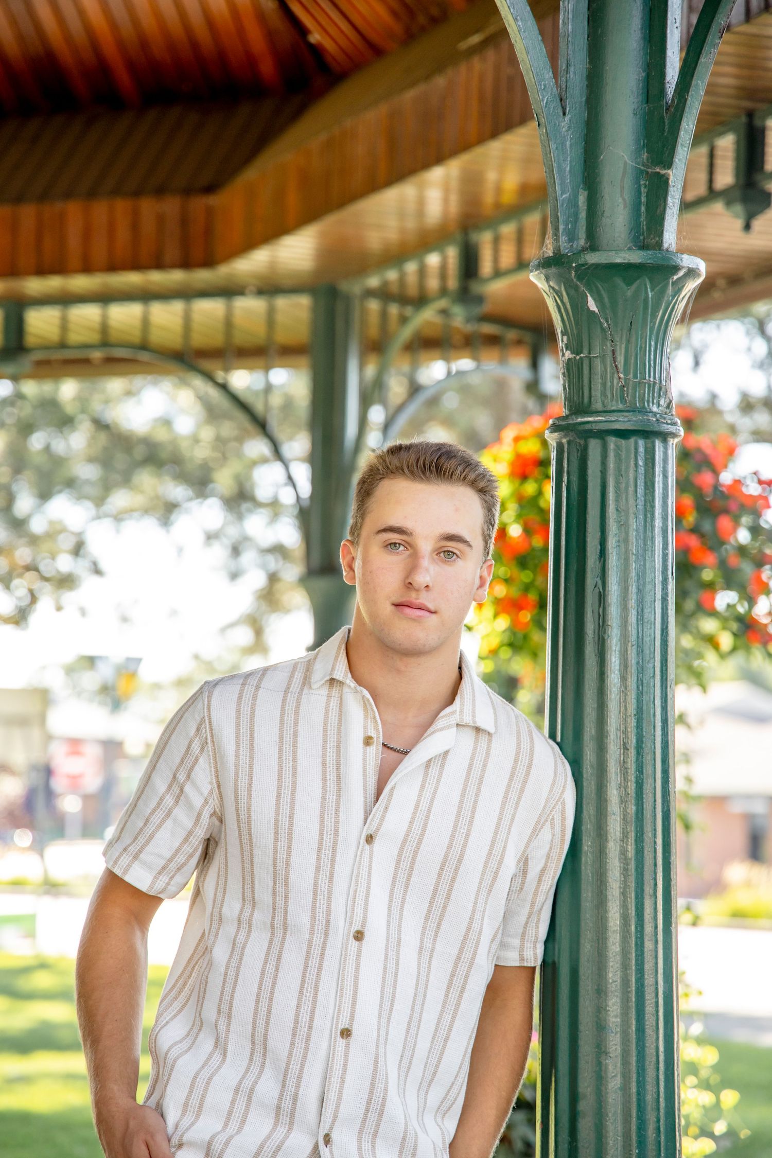 Person poses against green columns wearing striped button-down shirt in outdoor setting.