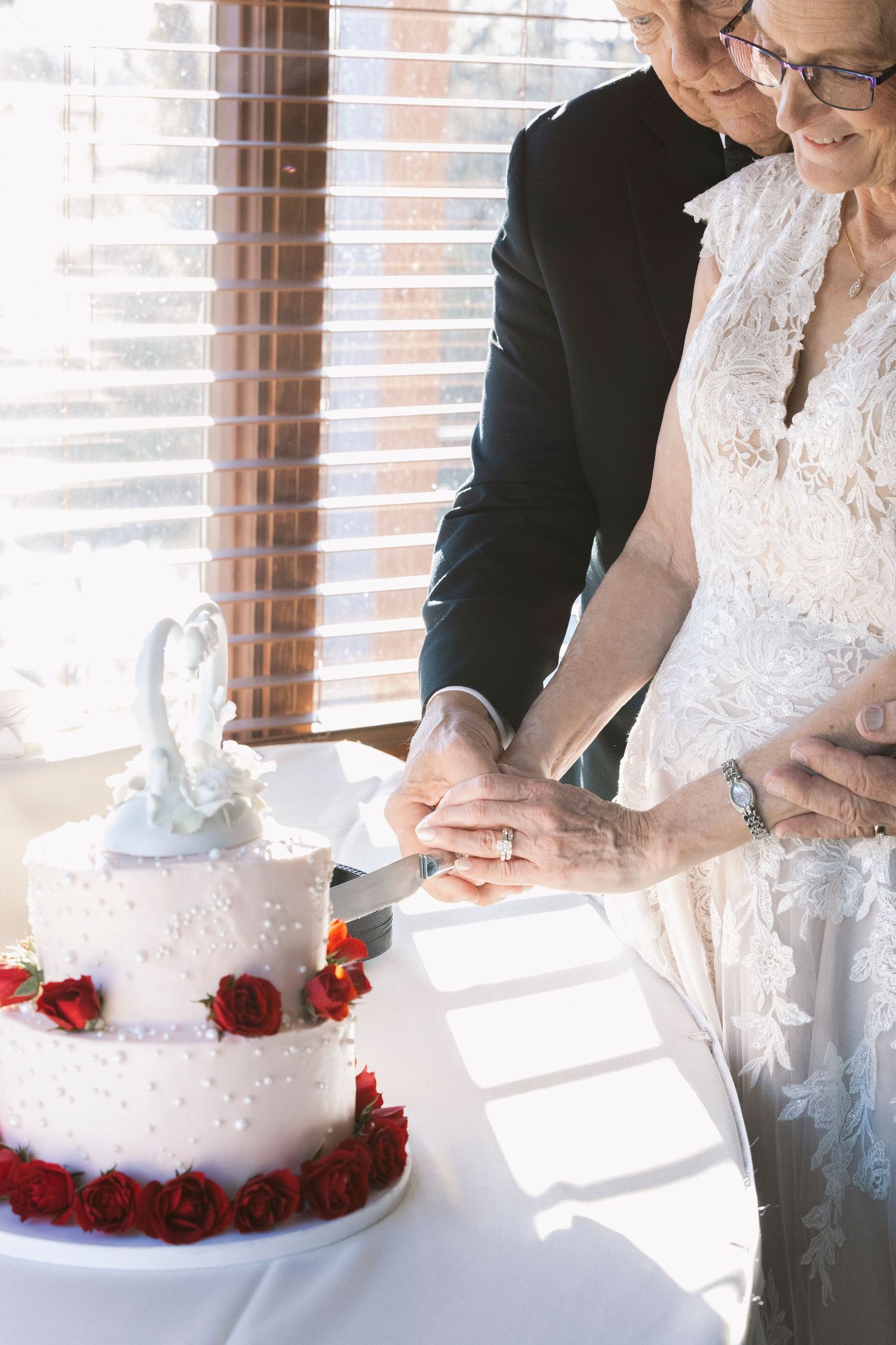 Newlyweds cutting their white wedding cake decorated with red roses.