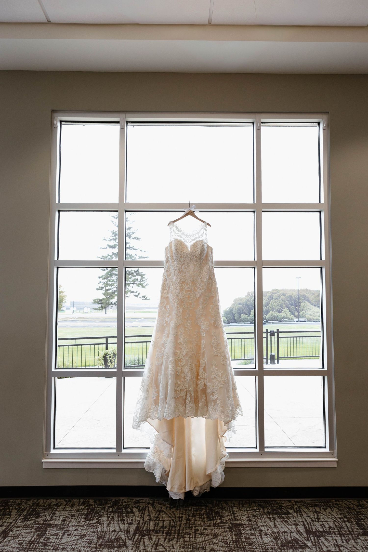 Wedding gown displayed against large windows with scenic countryside view.