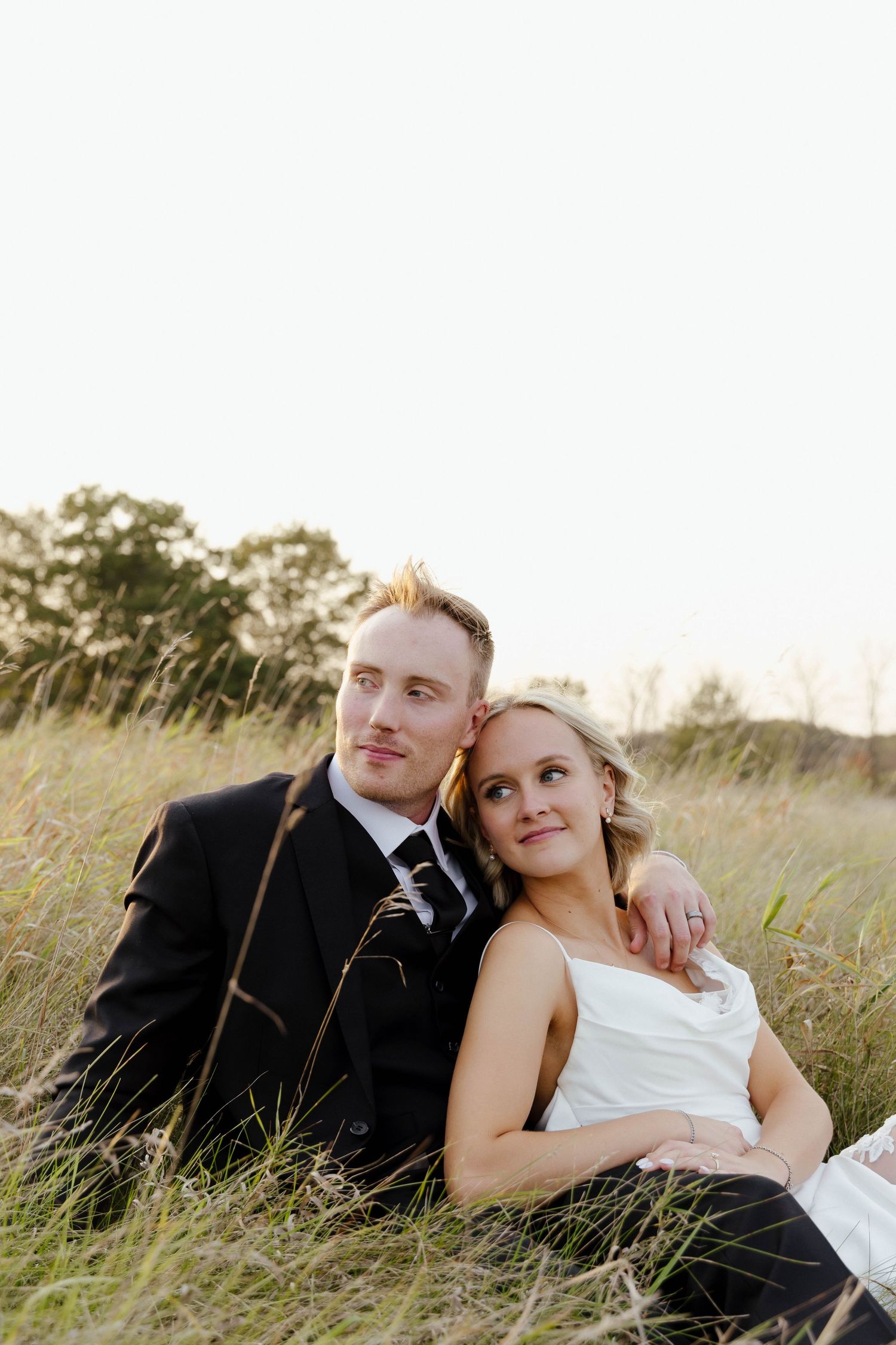Romantic couple lying in tall grass during sunset wedding photoshoot.