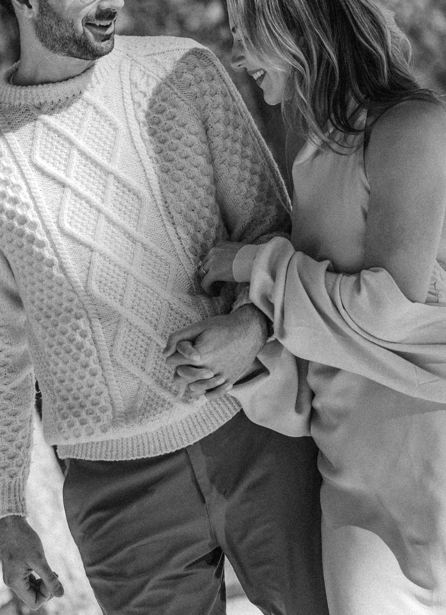 A romantic black and white close-up of a couple holding hands, with one wearing a cozy cable knit sweater.