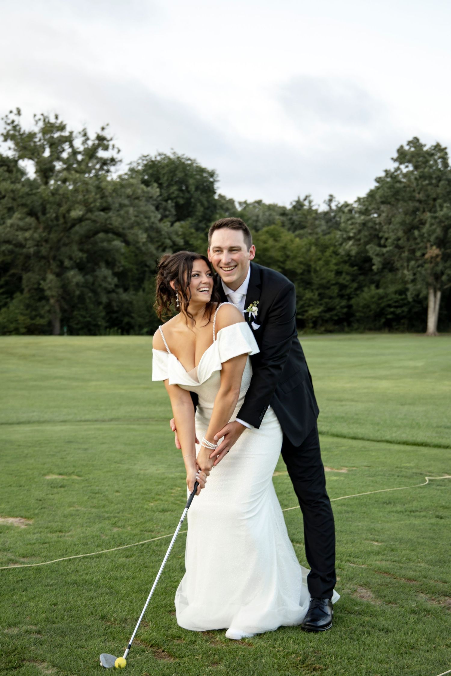 Playful wedding couple golfing together on a green course.
