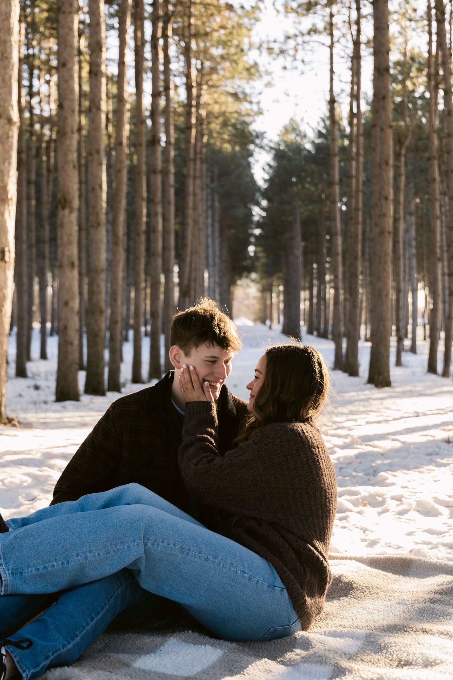 Couple lying in snow-covered forest ground sharing an intimate moment.