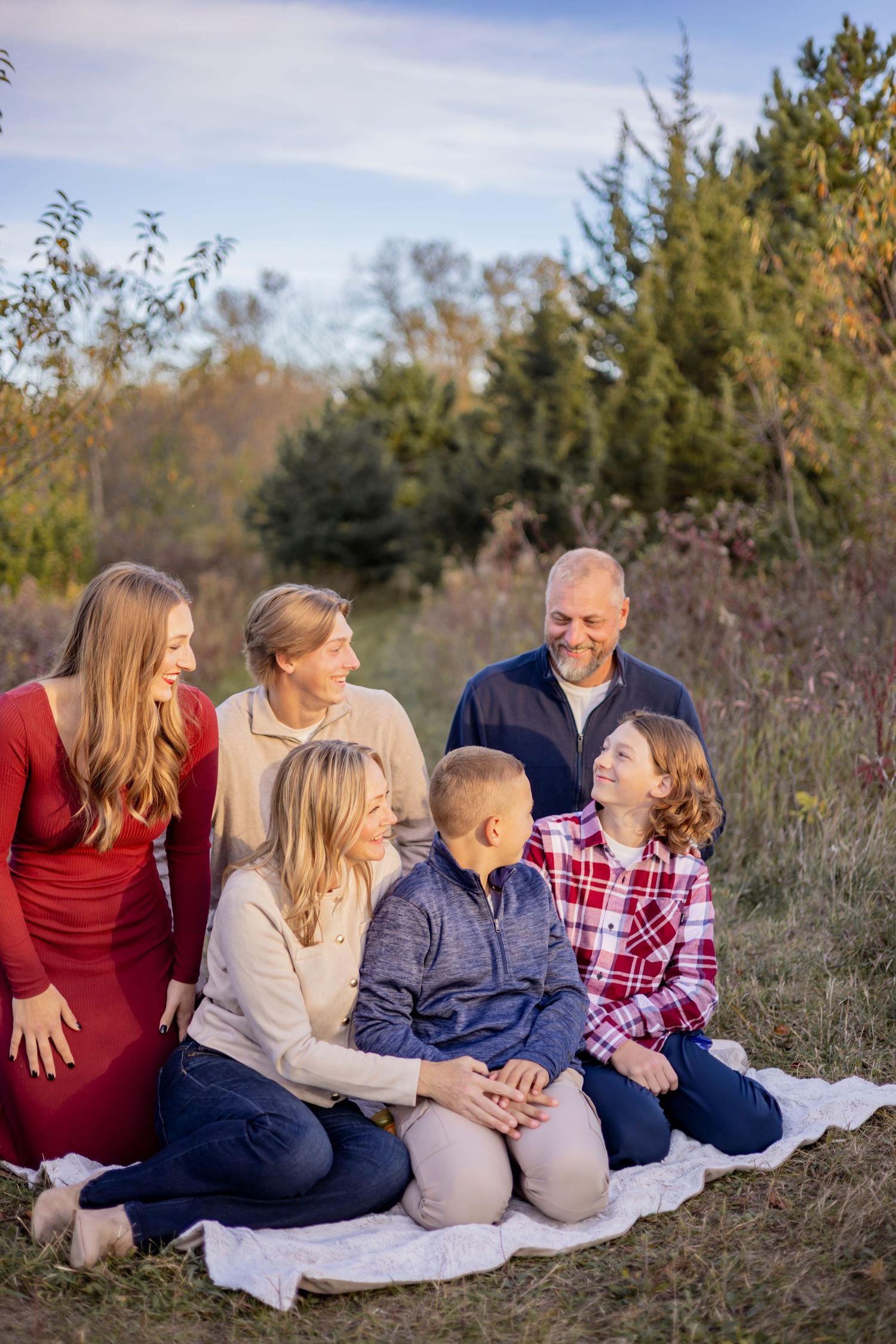 Family relaxes together on blanket during outdoor fall photoshoot with natural scenery.