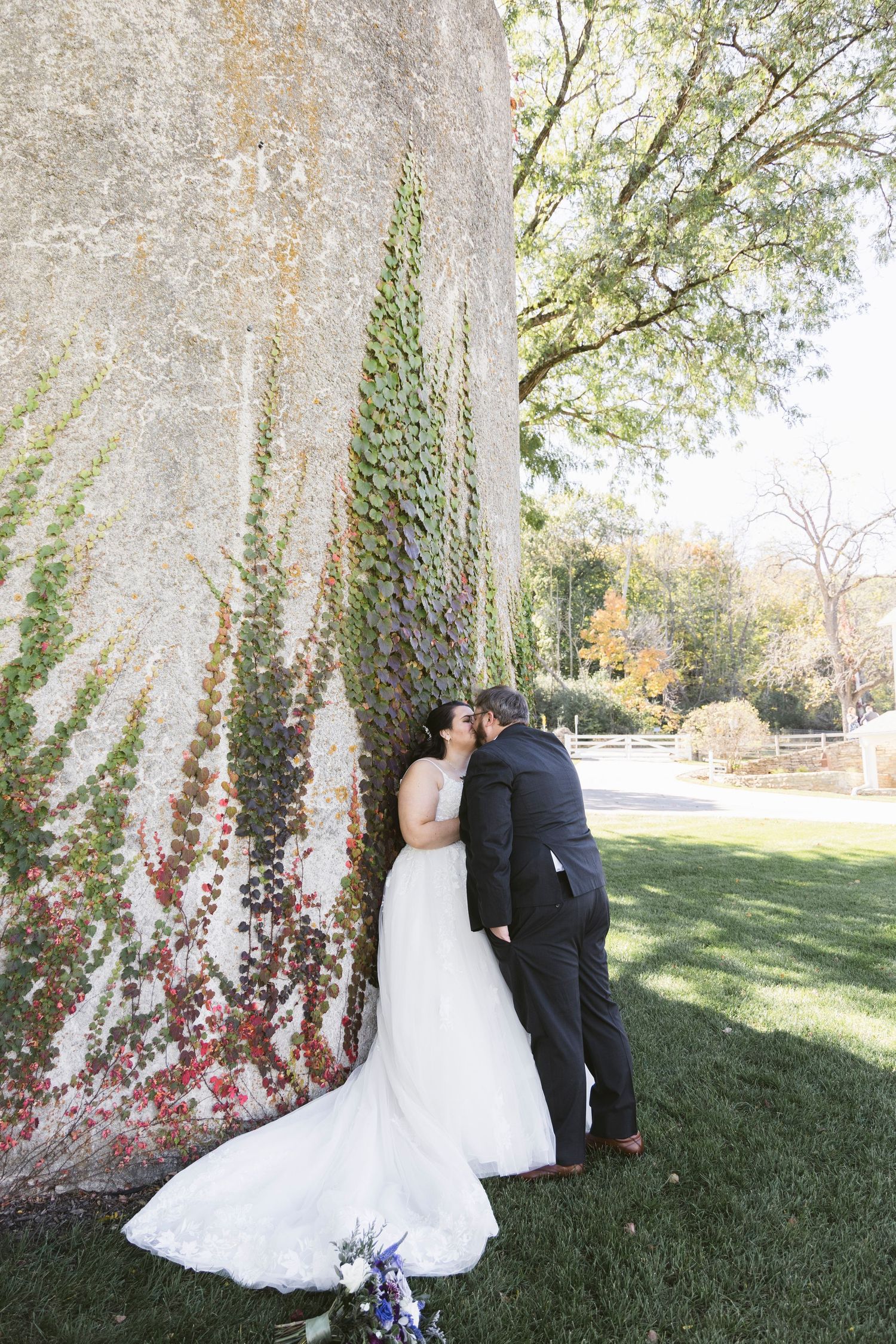 A romantic wedding photo series against a tree with ivy and red flowers in an outdoor setting.