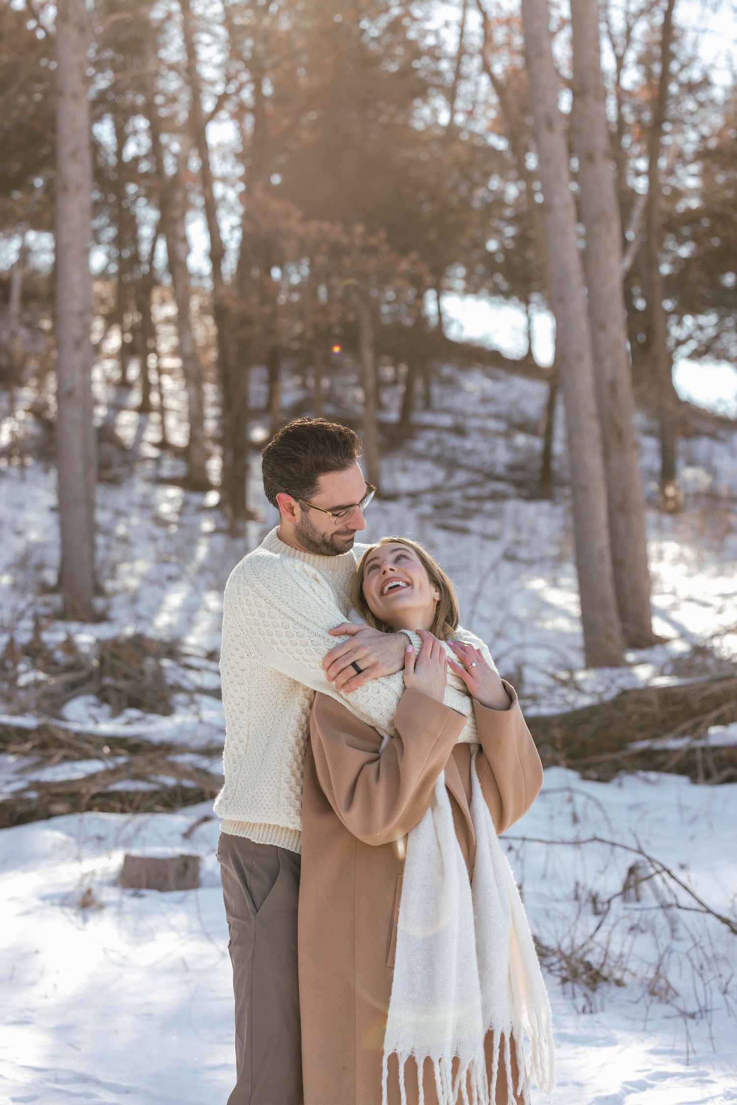 A tender winter embrace between a couple in warm sweaters surrounded by snow-covered trees.