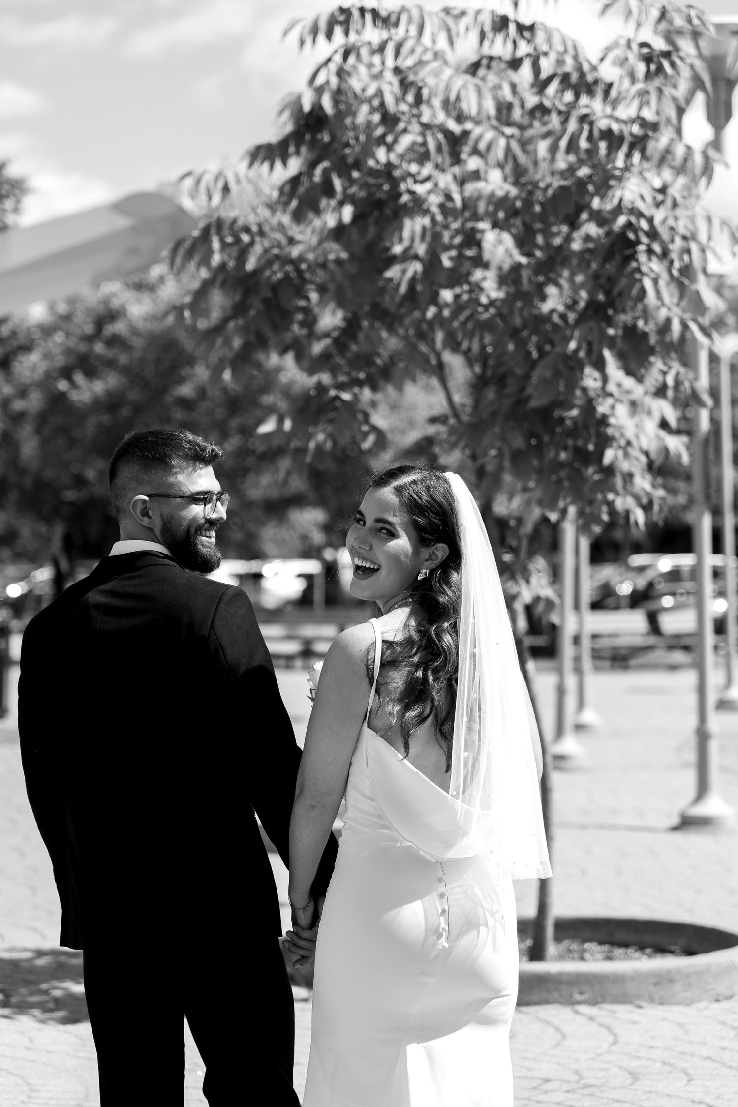 A wedding couple walks together in a black and white photo with trees in the background.