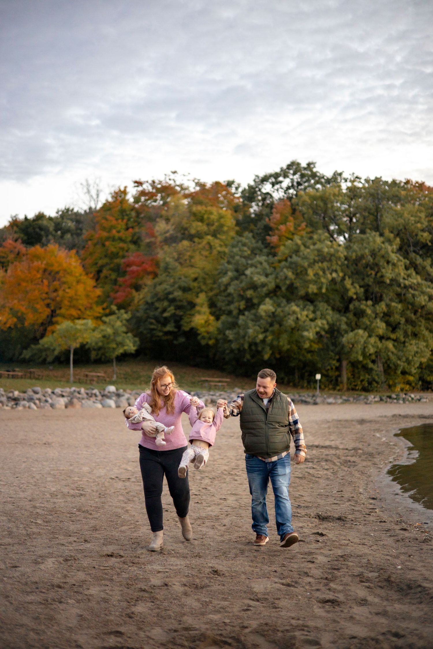 Family walking together on a sandy beach with autumn foliage in the background.