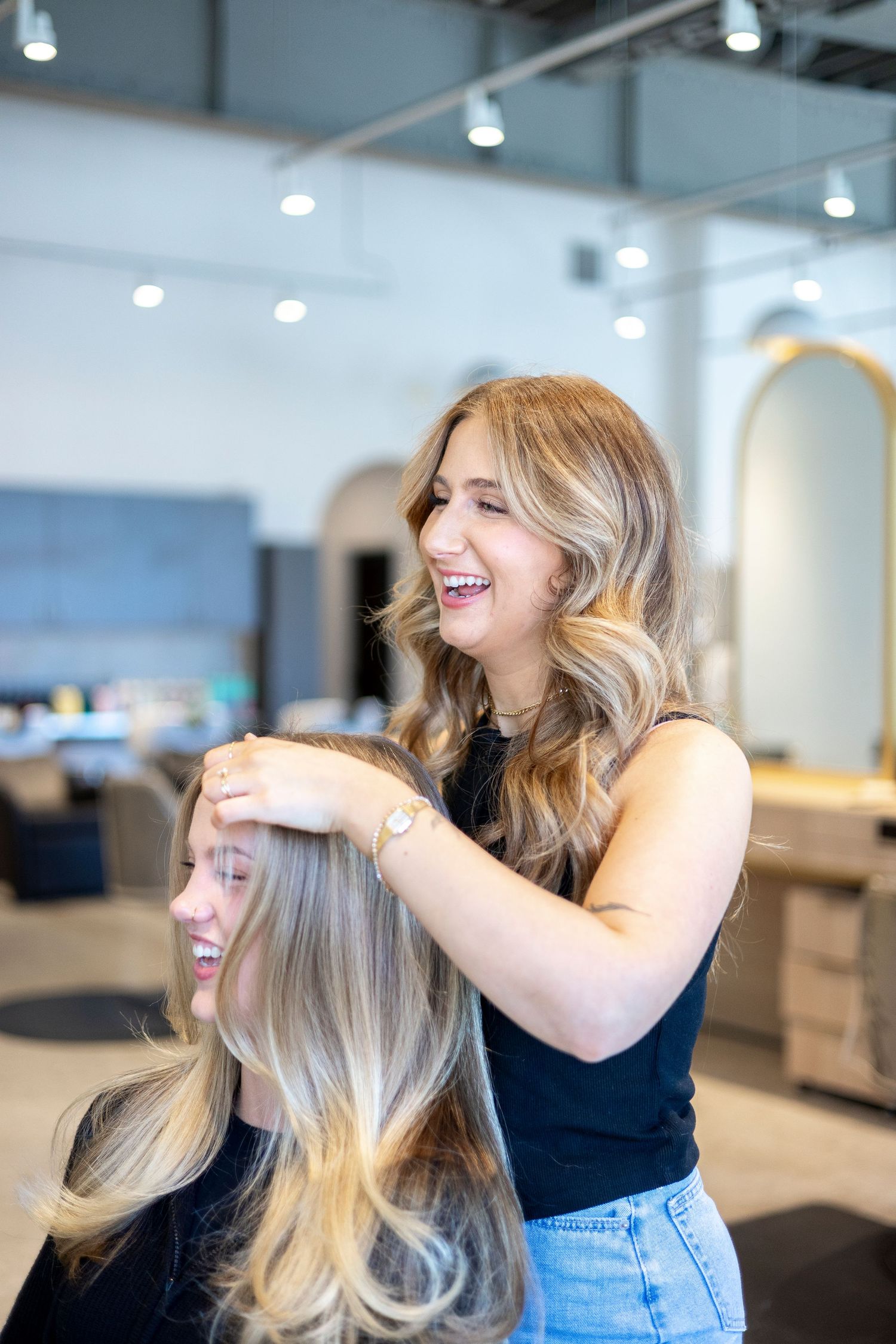 Hairstylist working on client's blonde hair in contemporary salon space.
