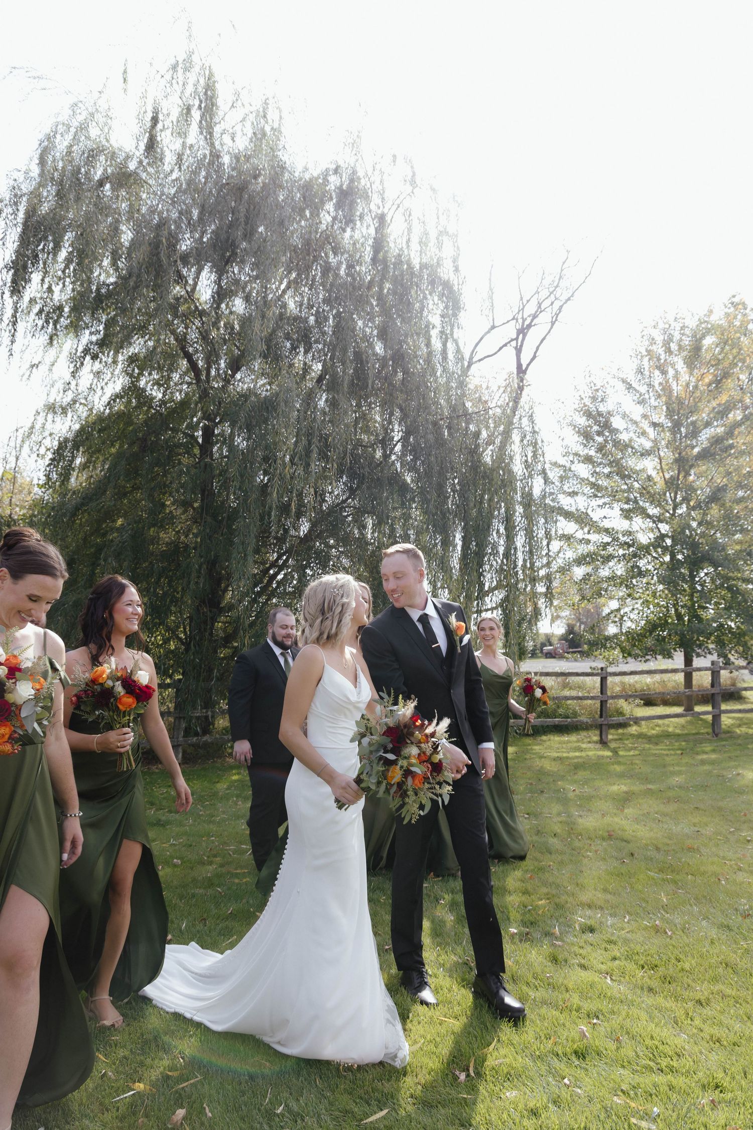 Wedding party celebrating outdoors with bouquets against natural landscape.
