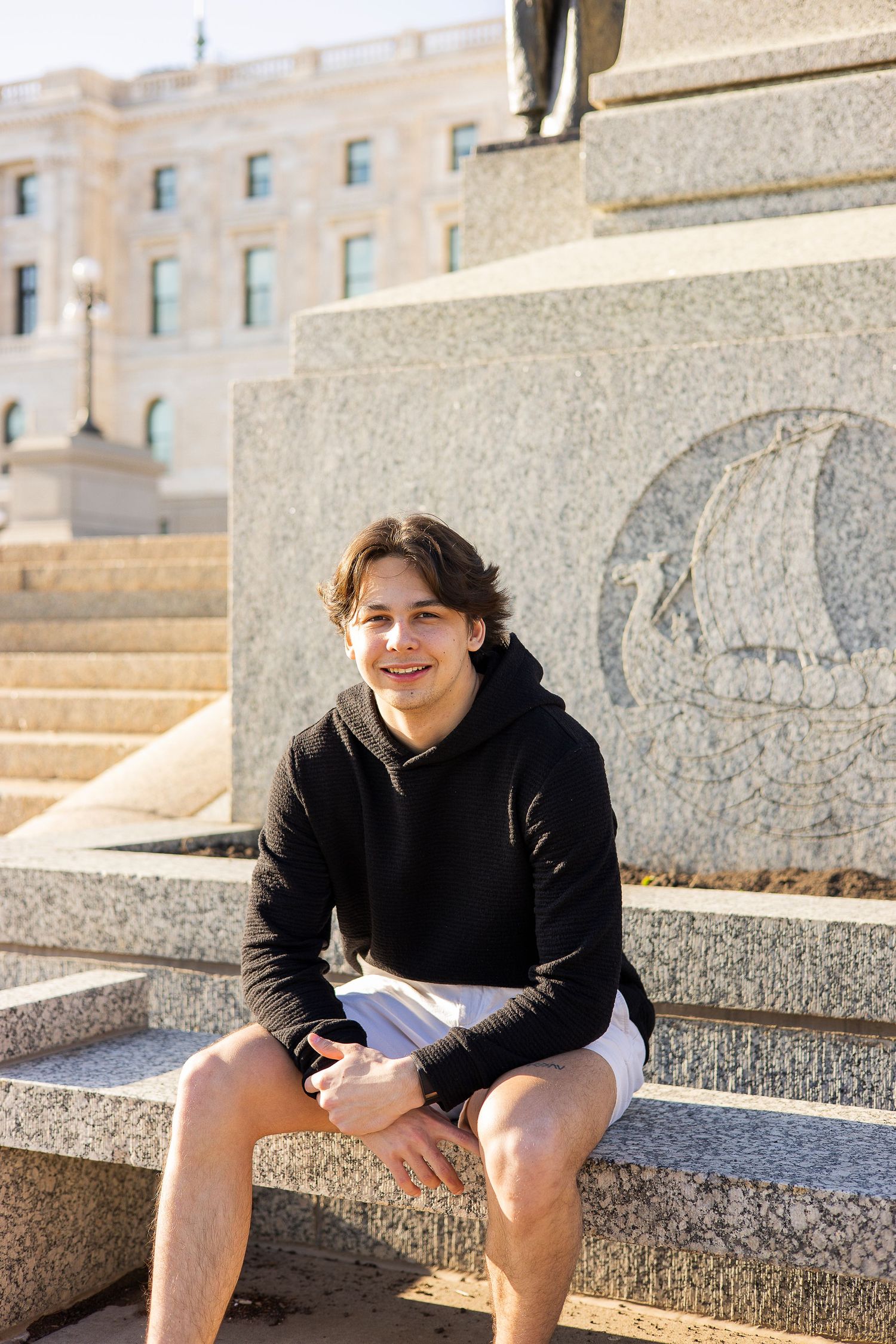 Person relaxing on stone steps of historic government building in casual attire.