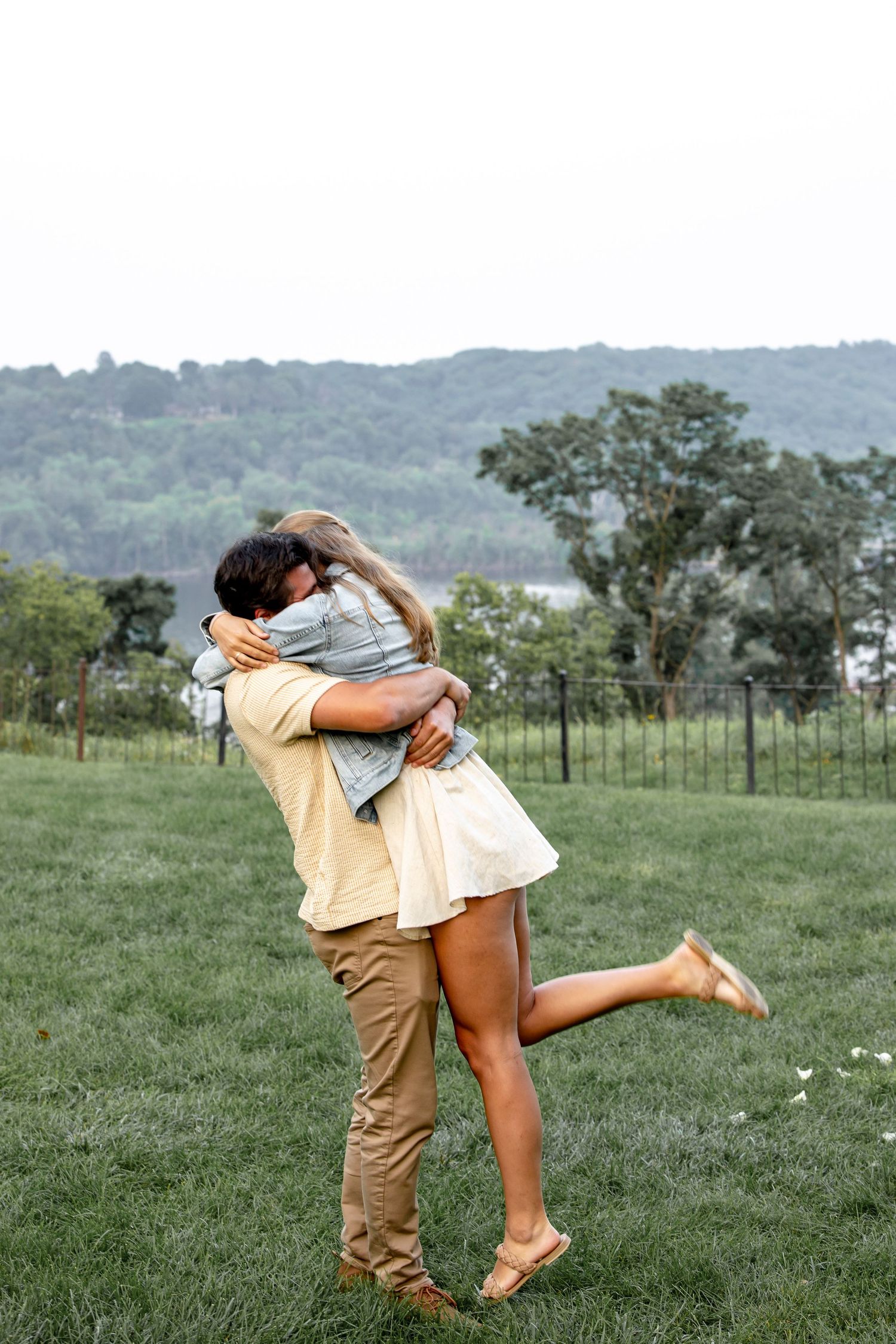 Playful couple embracing in a sunny meadow with rolling hills in the background.