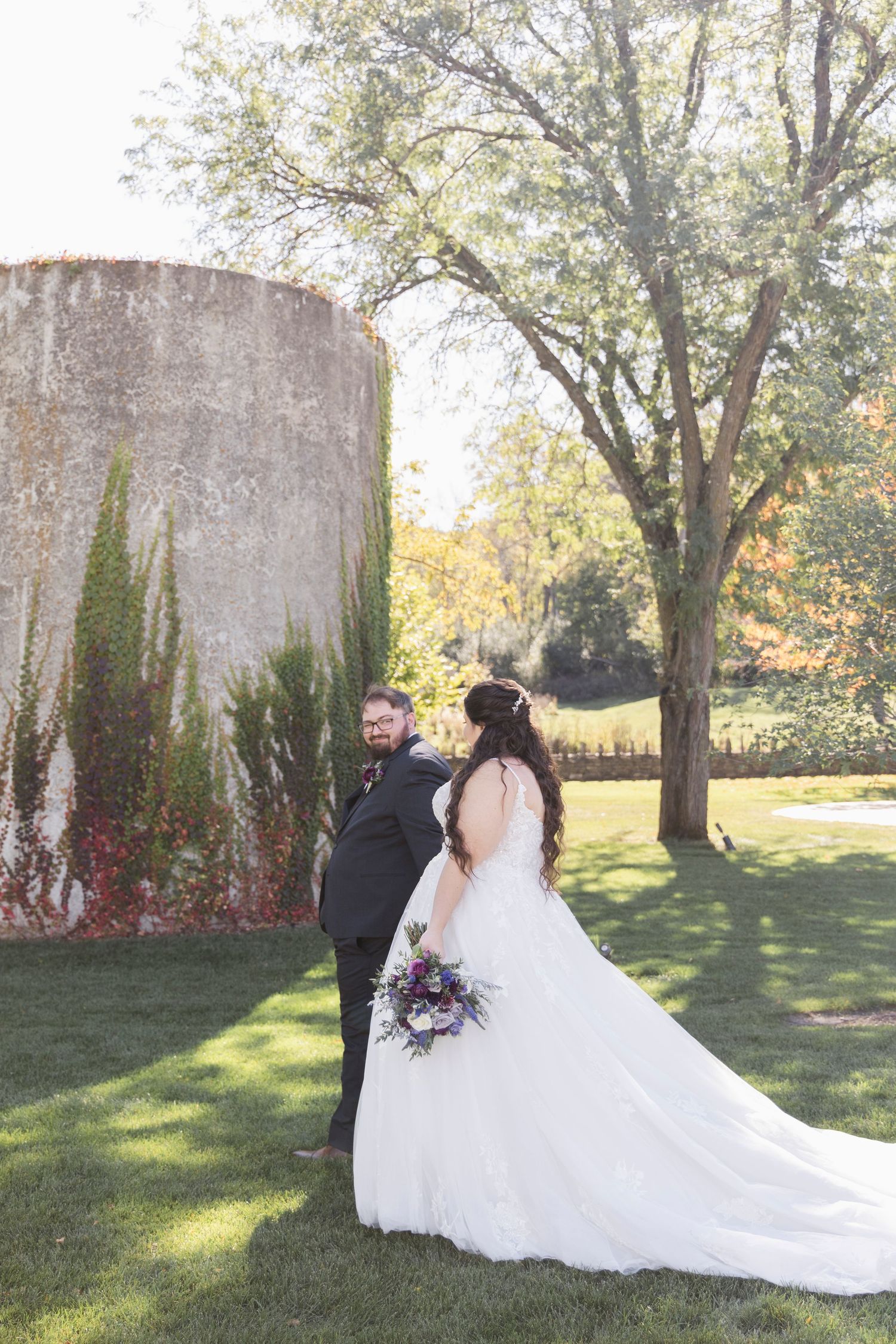 Wedding couple photographed in a garden setting with long white dress train against stone pillars.
