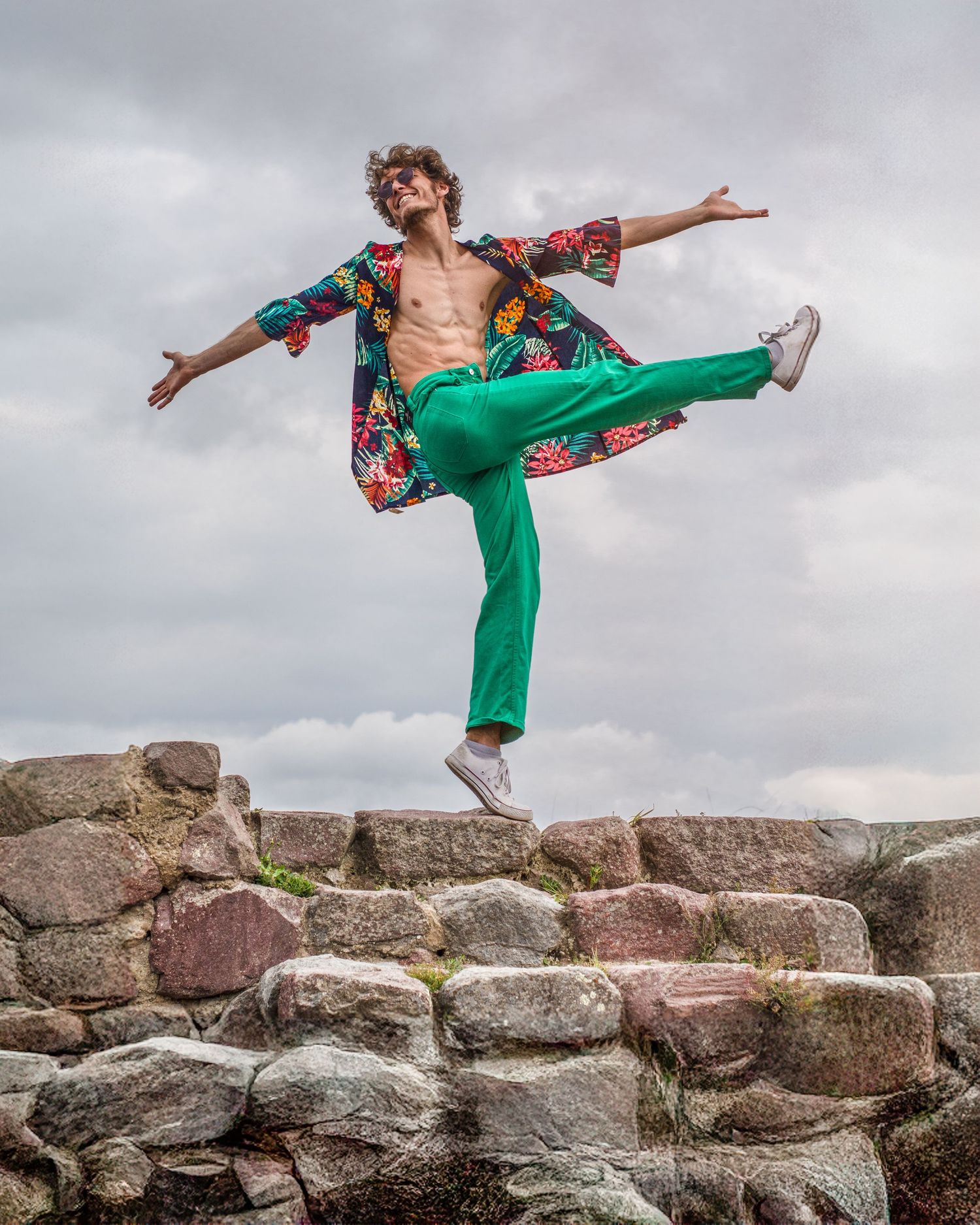 Dance sequence in green outfit performing balanced poses on stone wall.