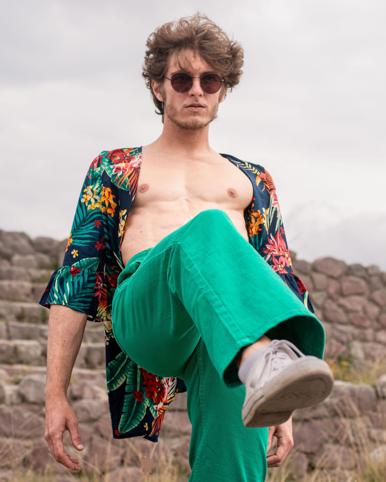 Model poses in a vibrant green outfit with floral print jacket against a rocky outdoor backdrop.