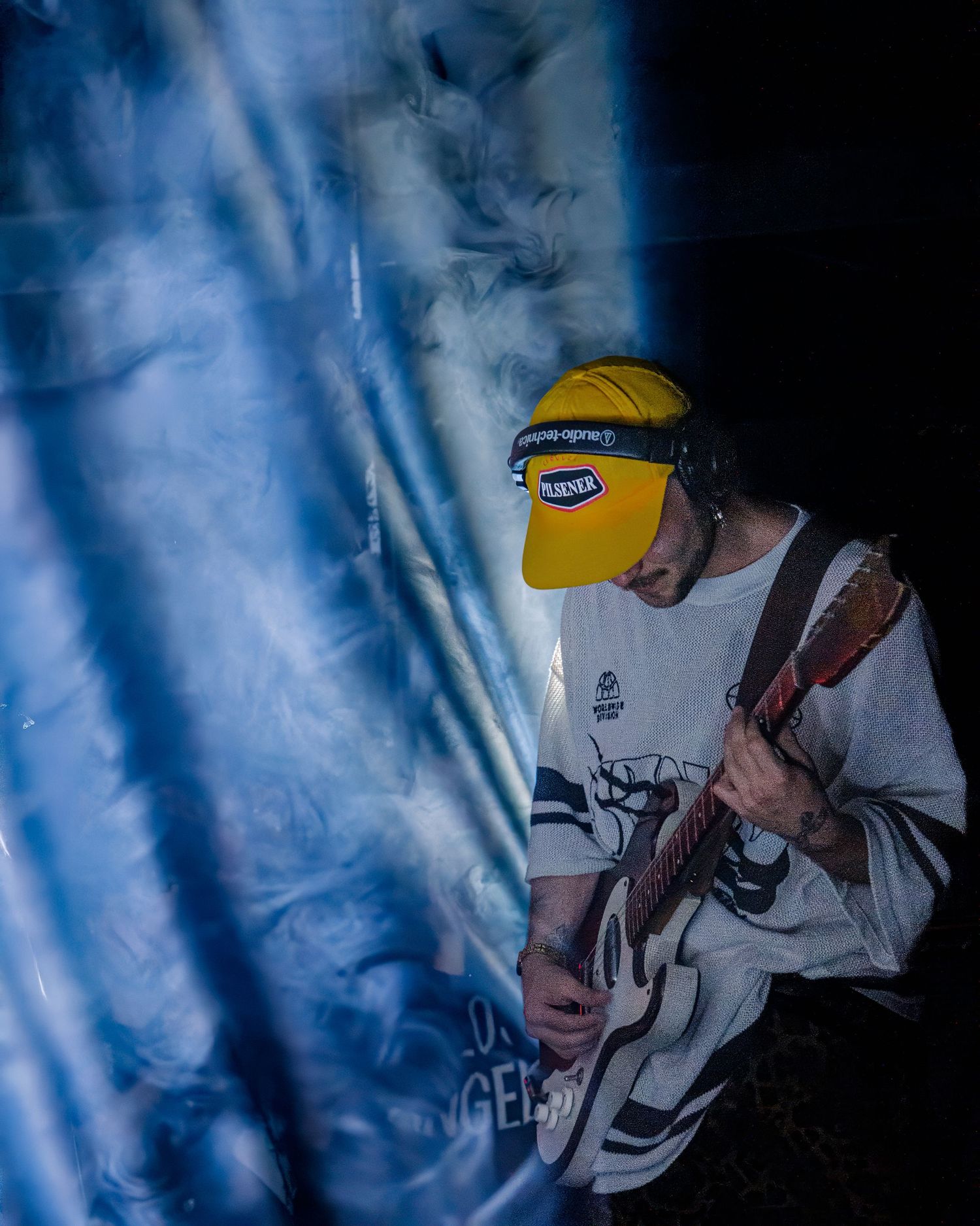 Performer in yellow cap and white jacket captured in moody blue stage lighting.