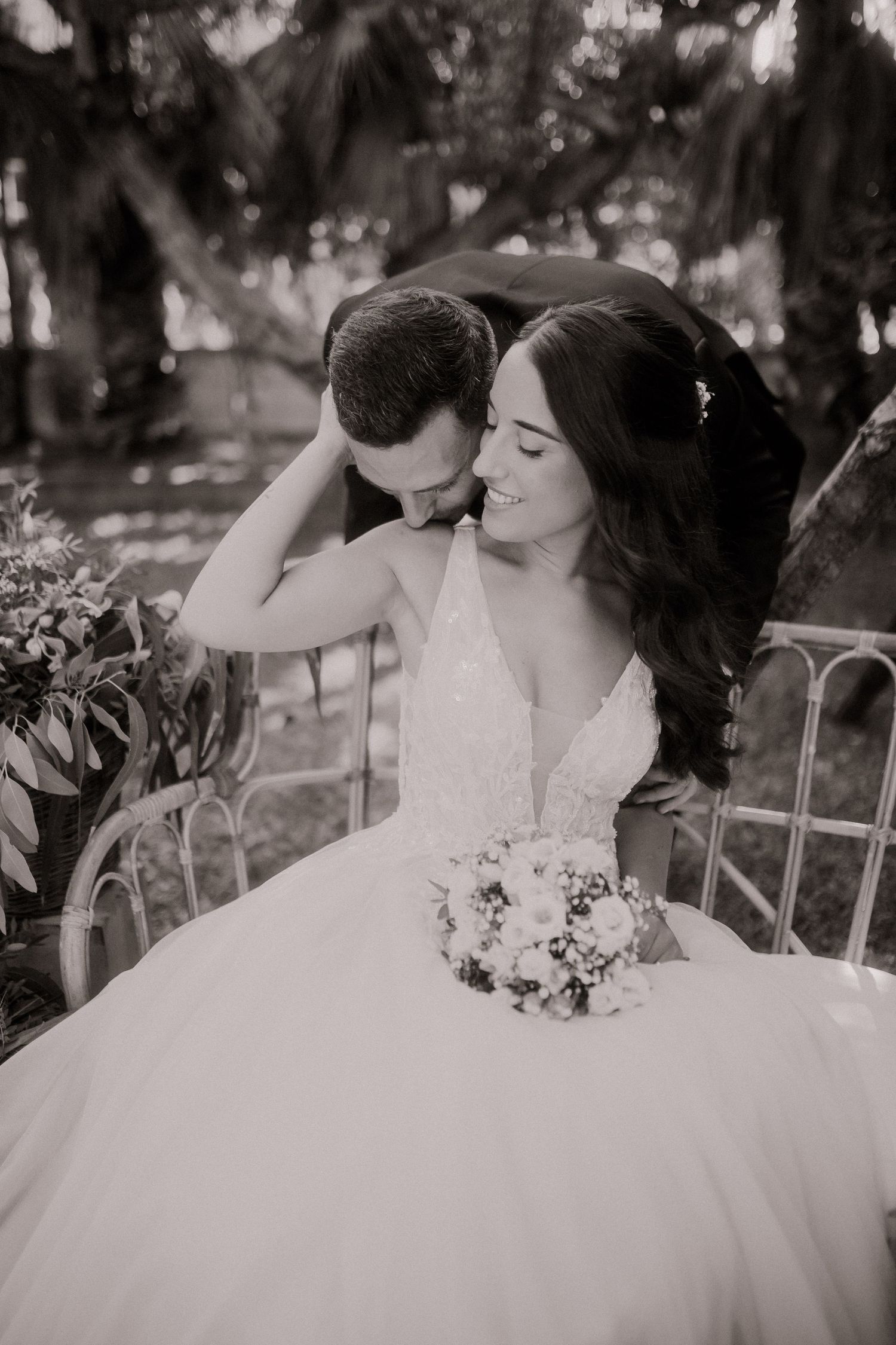 Novio besando el hombro de la novia sentada en banco en fotografía de boda en blanco y negro en Tarragona