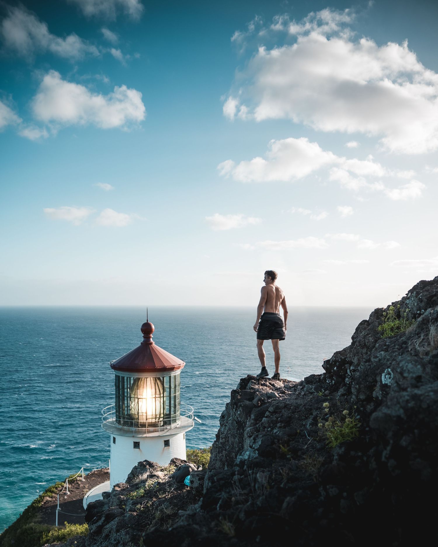 Historic lighthouse perched on rocky coastal cliff overlooking turquoise ocean waters.