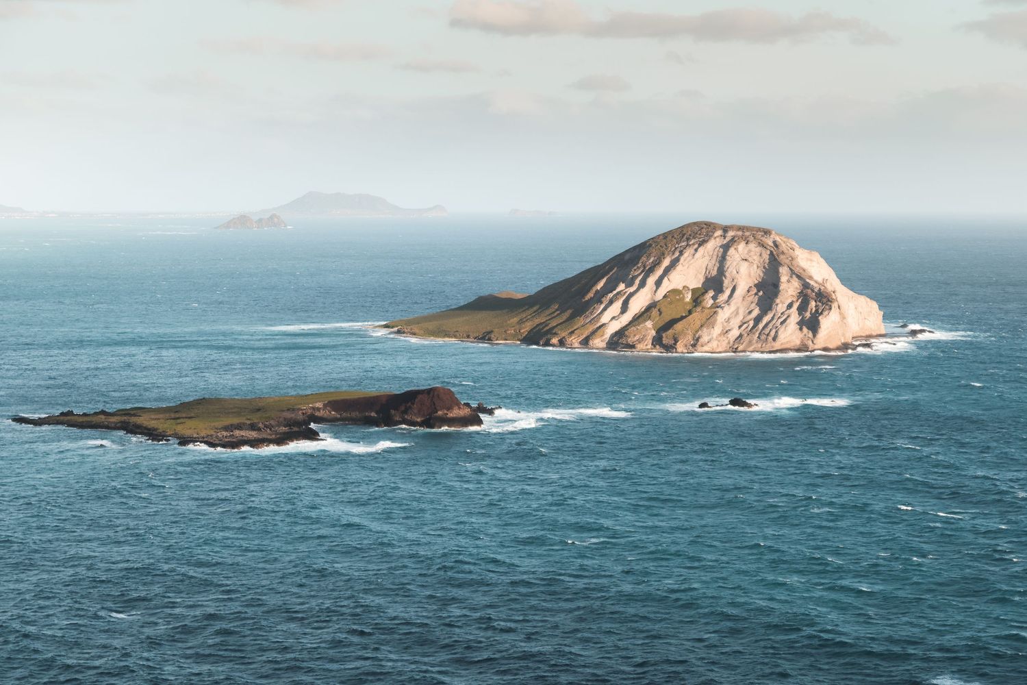 A rugged, rocky island rises from the tranquil ocean, surrounded by crashing waves and a serene horizon In Hawaii.