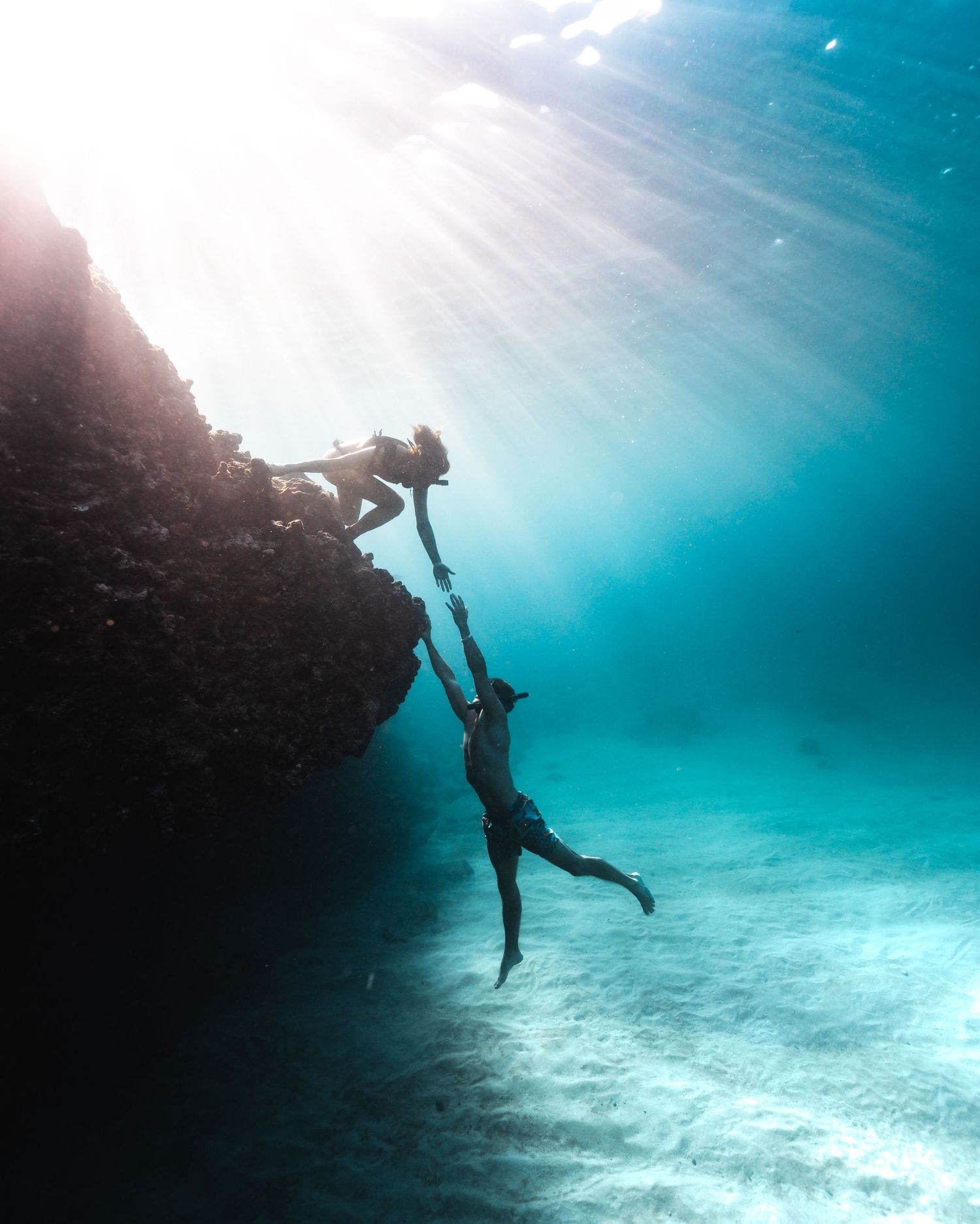 Underwater silhouettes diving and swimming in clear blue ocean waters.