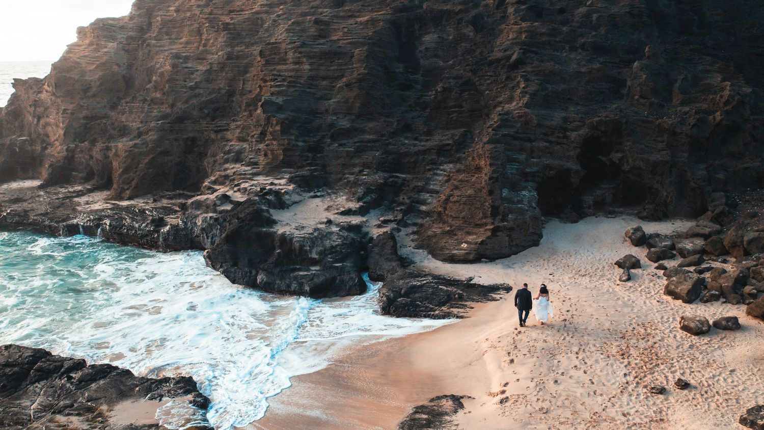 Panoramic view of rugged volcanic coastline with sandy beach and ocean waves.