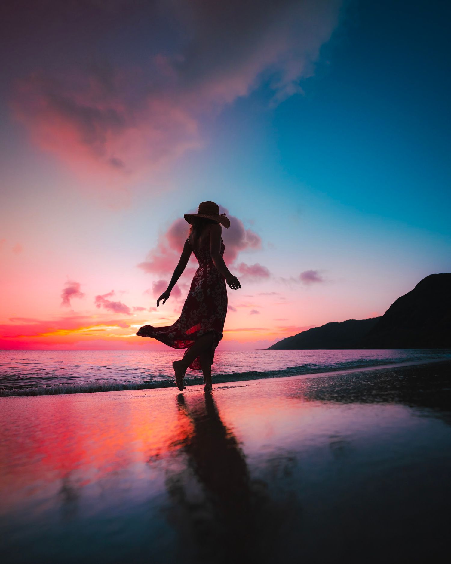 Silhouette against vibrant pink and orange sunset sky on a reflective beach.
