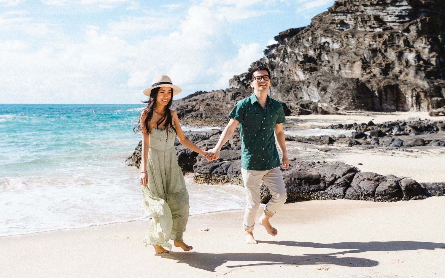 Couple holding hands while walking along dramatic rocky beach coastline.