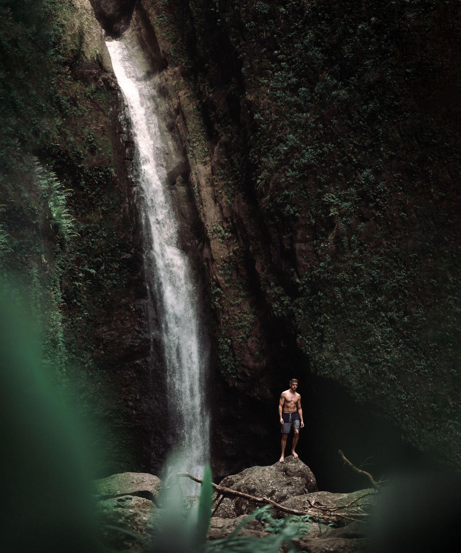 A dramatic waterfall cascades down a rocky cliff face in a lush tropical setting.