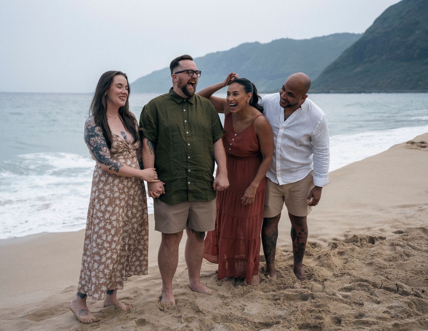 Group gathering on scenic beach with mountains and waves in background.