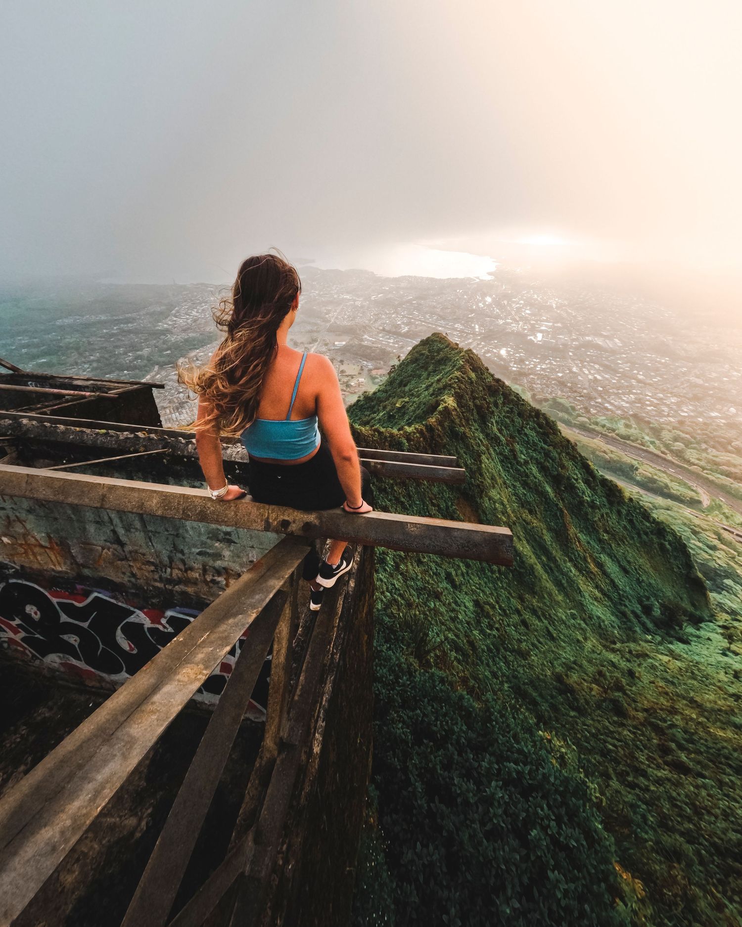 Person sitting on wooden stairs overlooking a misty mountain ridge at sunrise.