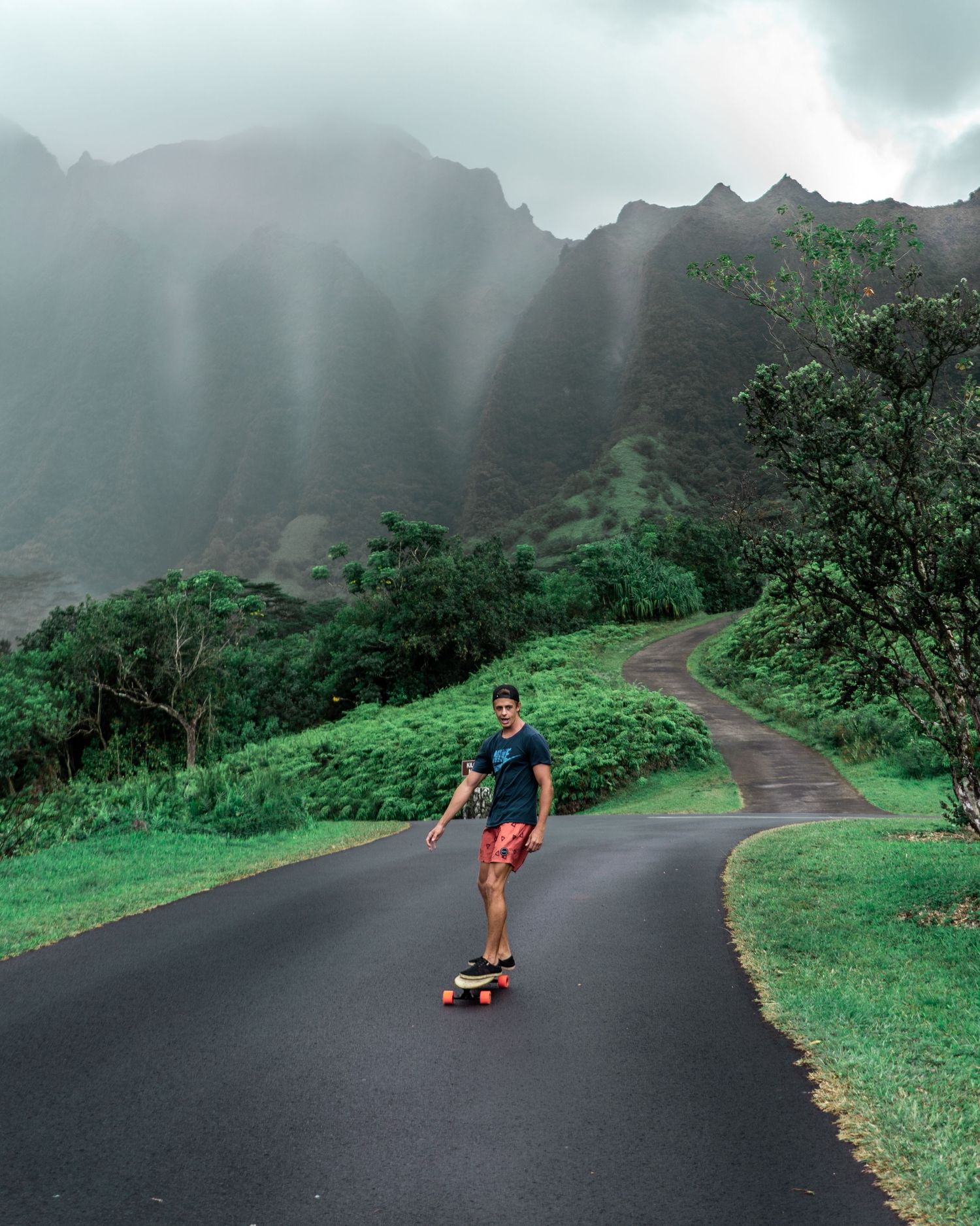 Longboarder skating down a winding mountain road surrounded by lush greenery.