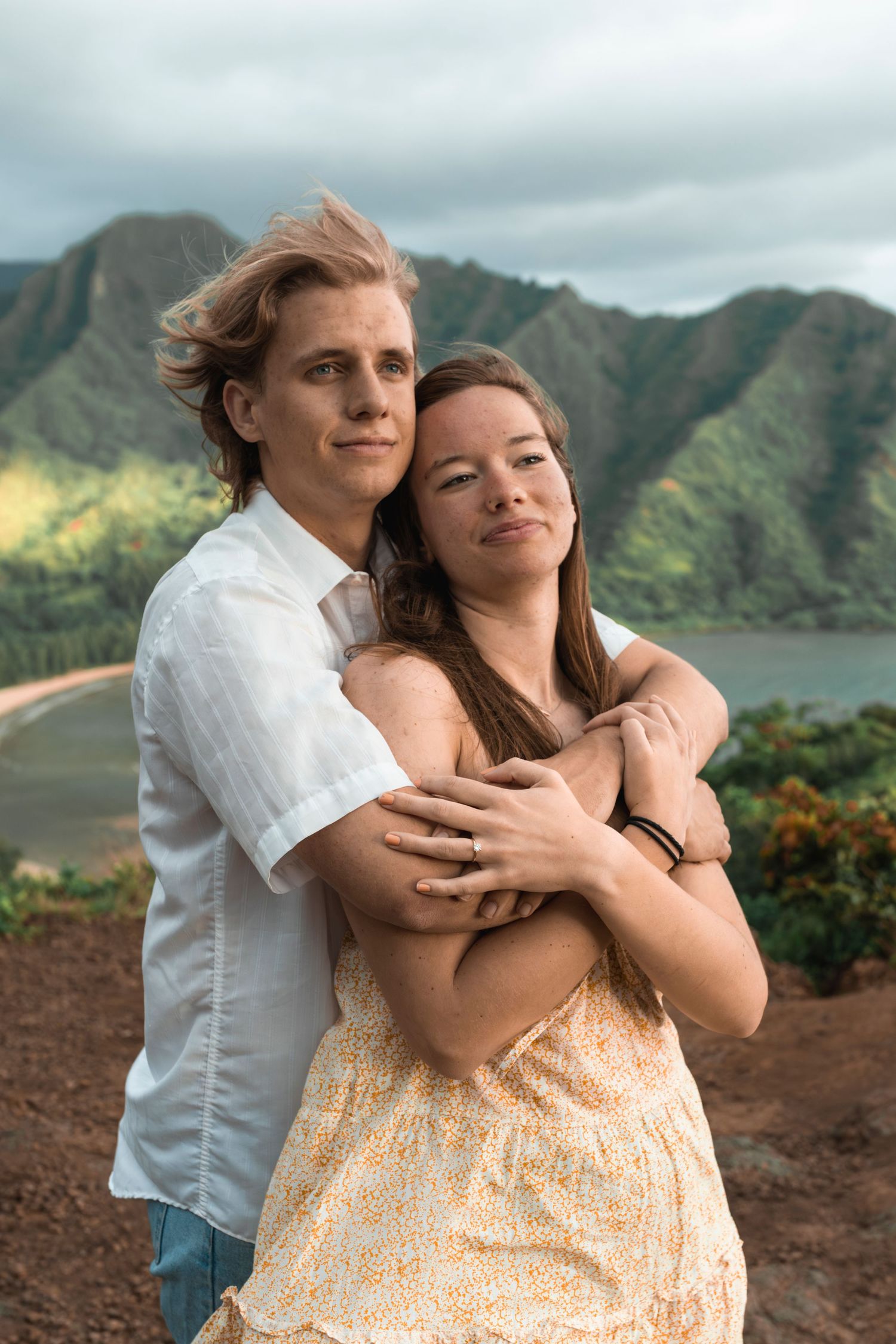 A tender embrace shared on a scenic mountain overlook with ocean views in the background.