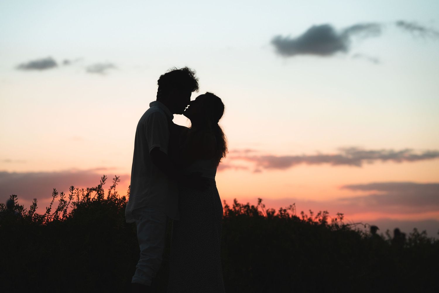 Silhouettes against a colorful sunset sky with clouds on the horizon.