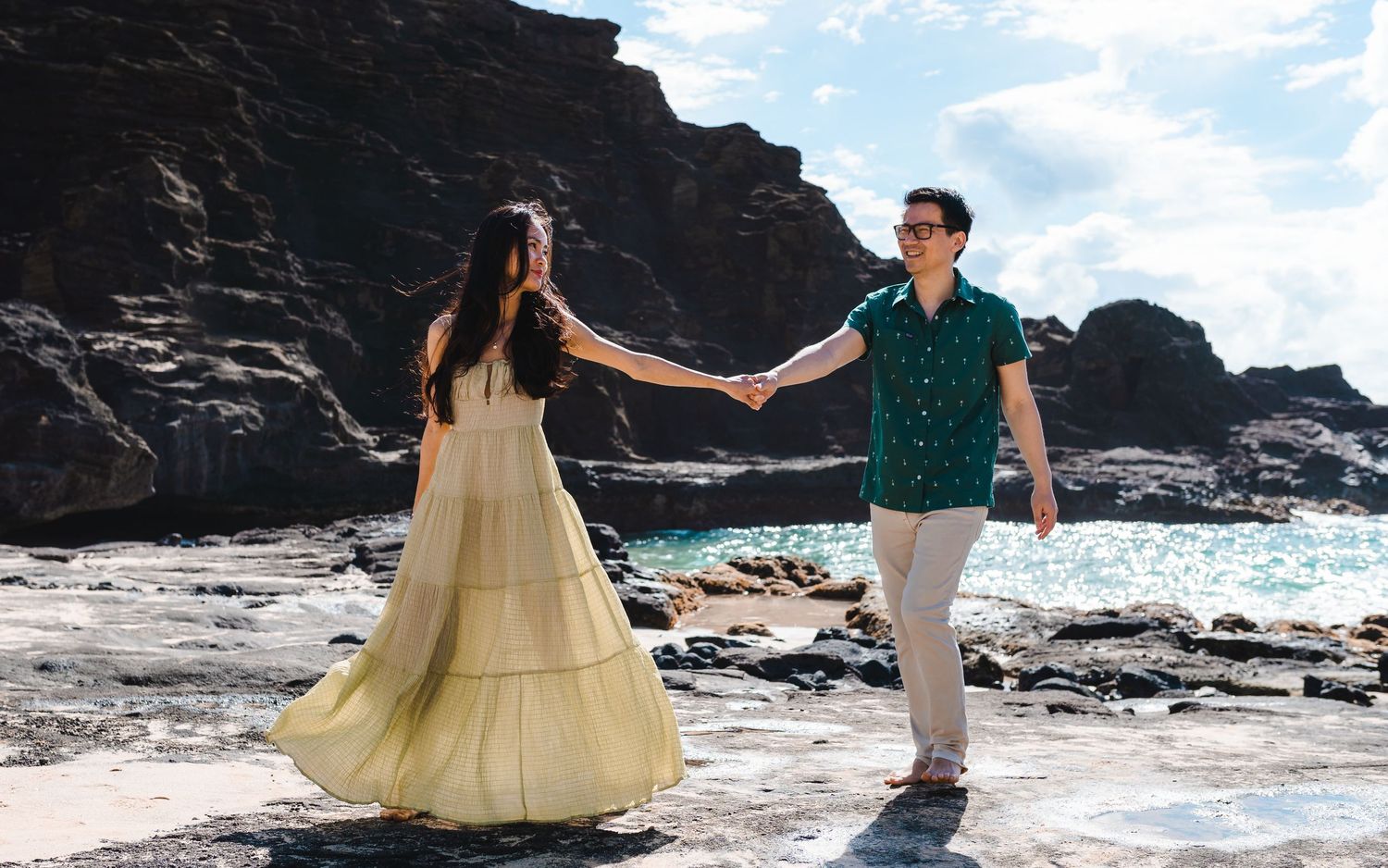 Couple dancing joyfully on a scenic beach with dramatic rocky cliffs in Hawaii.