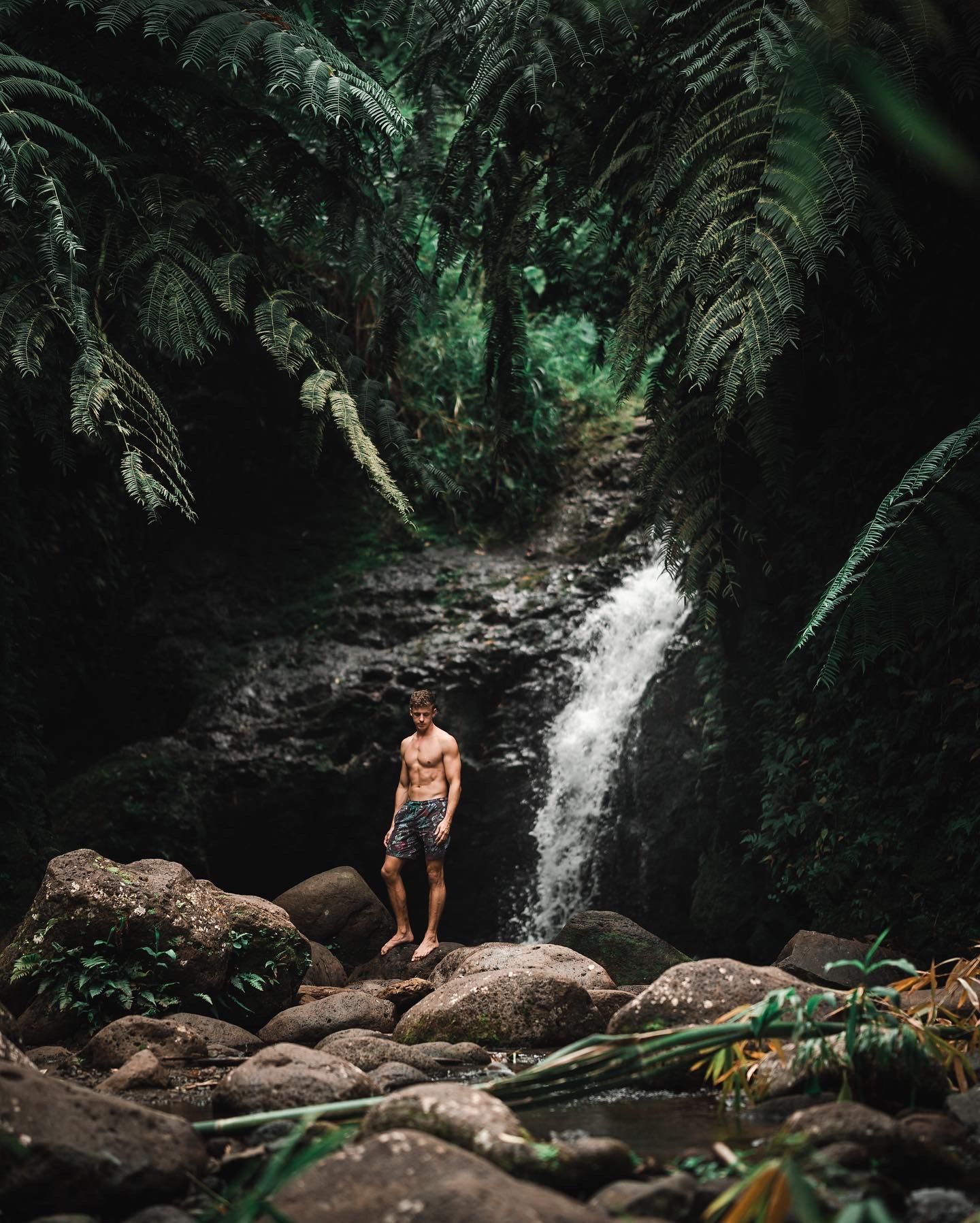 Waterfall cascading into a rocky stream bed surrounded by tropical foliage.
